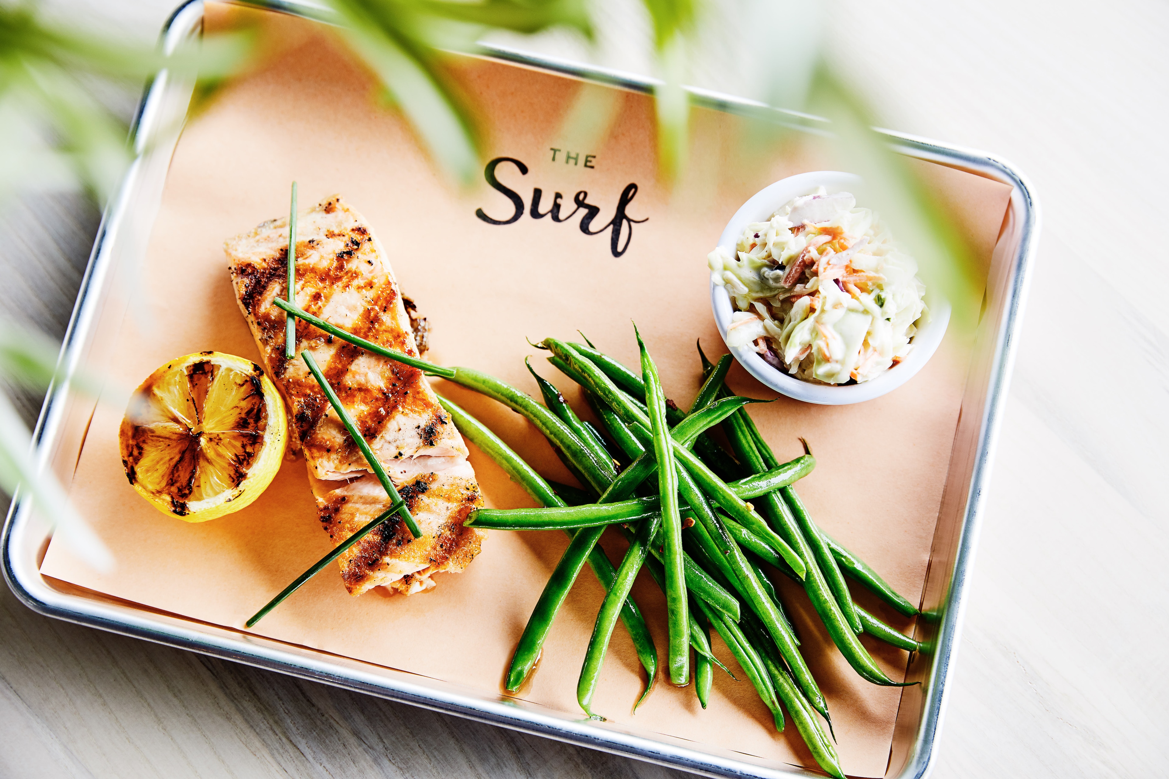 a plated dish of grilled chicken, green beans, and coleslaw on a metal tray