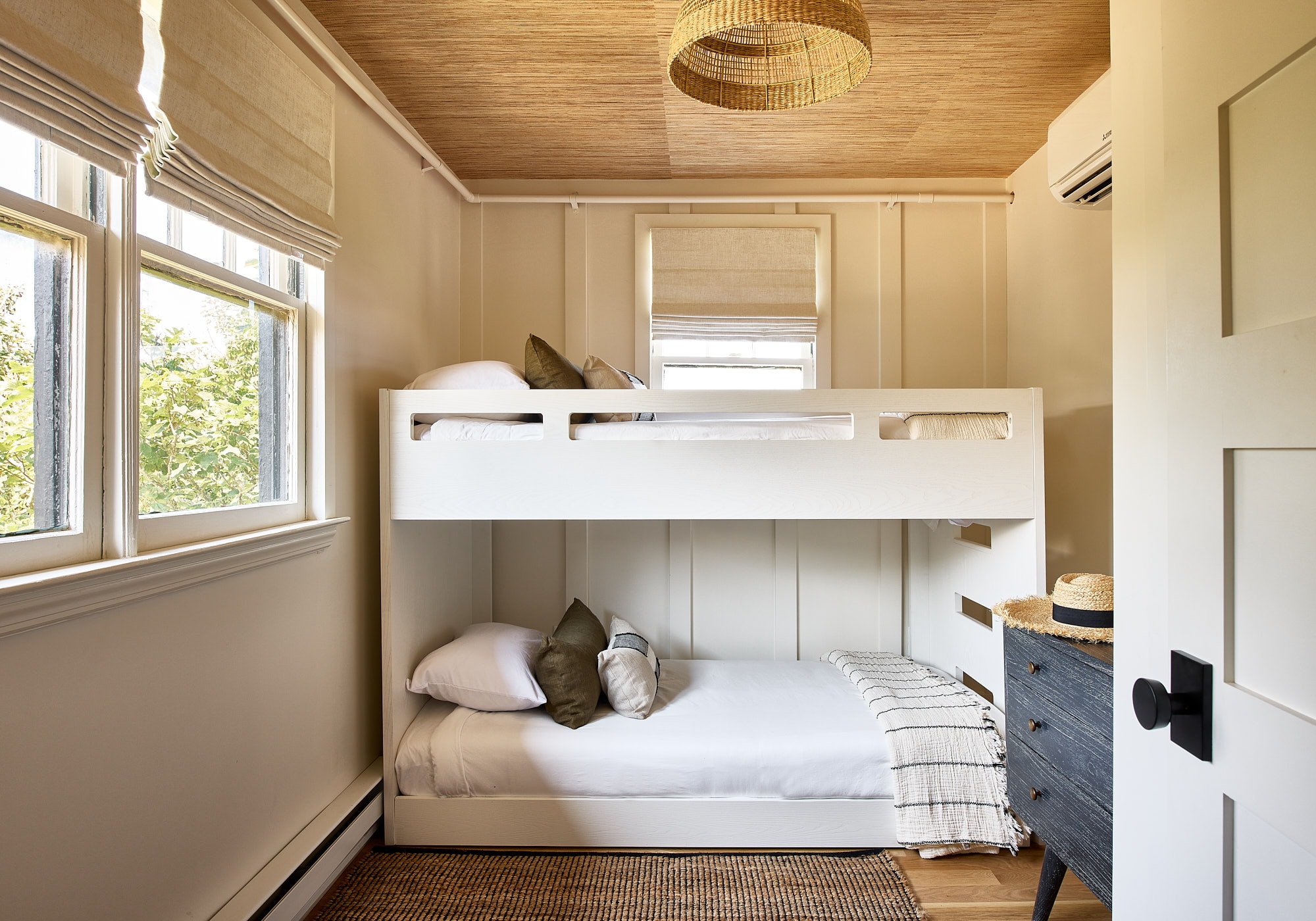 A small room with bunk beds, a window showing greenery outside, and a wooden ceiling.