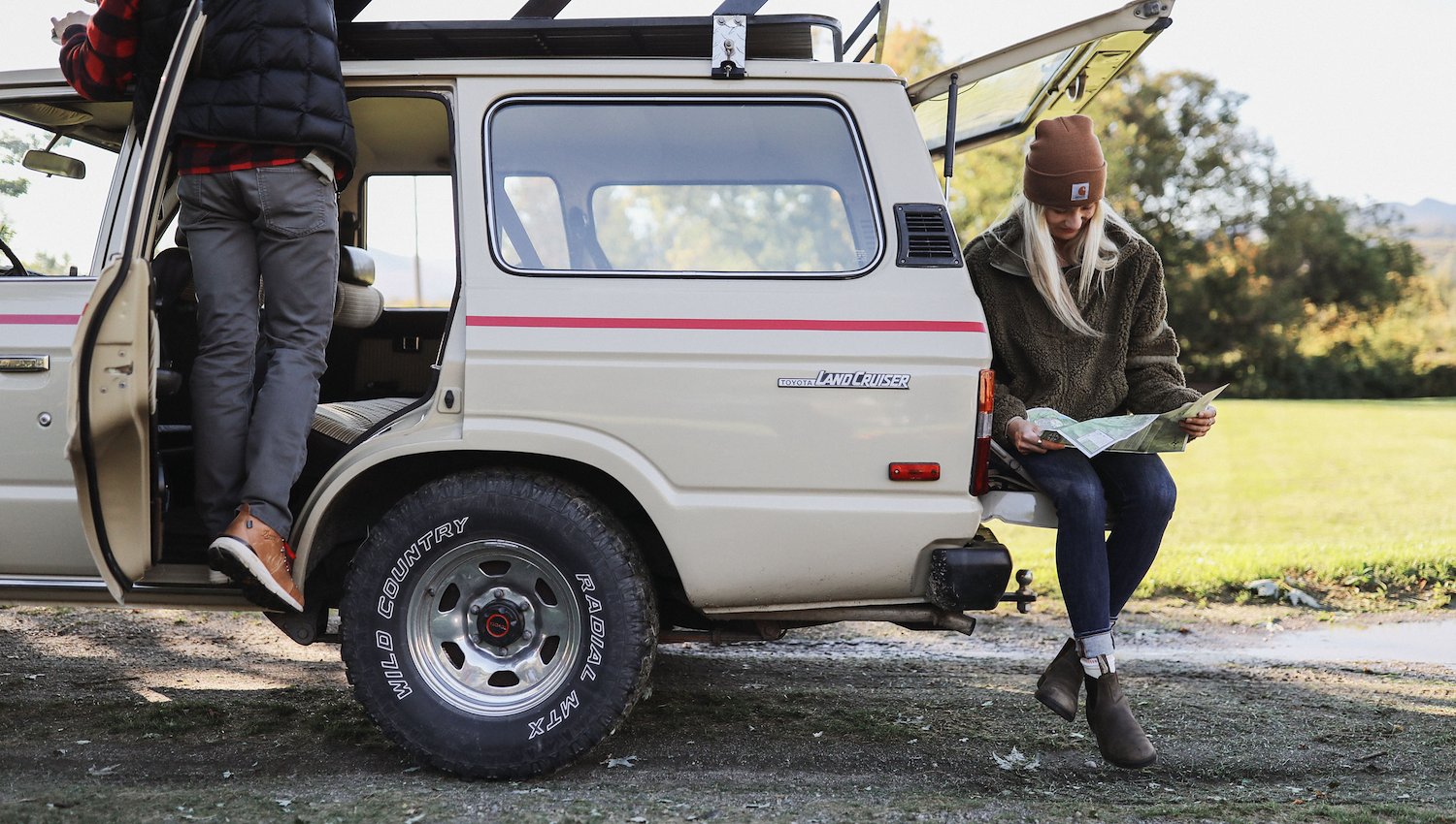 Travelers planning an outdoor adventure beside a vintage SUV with a map.