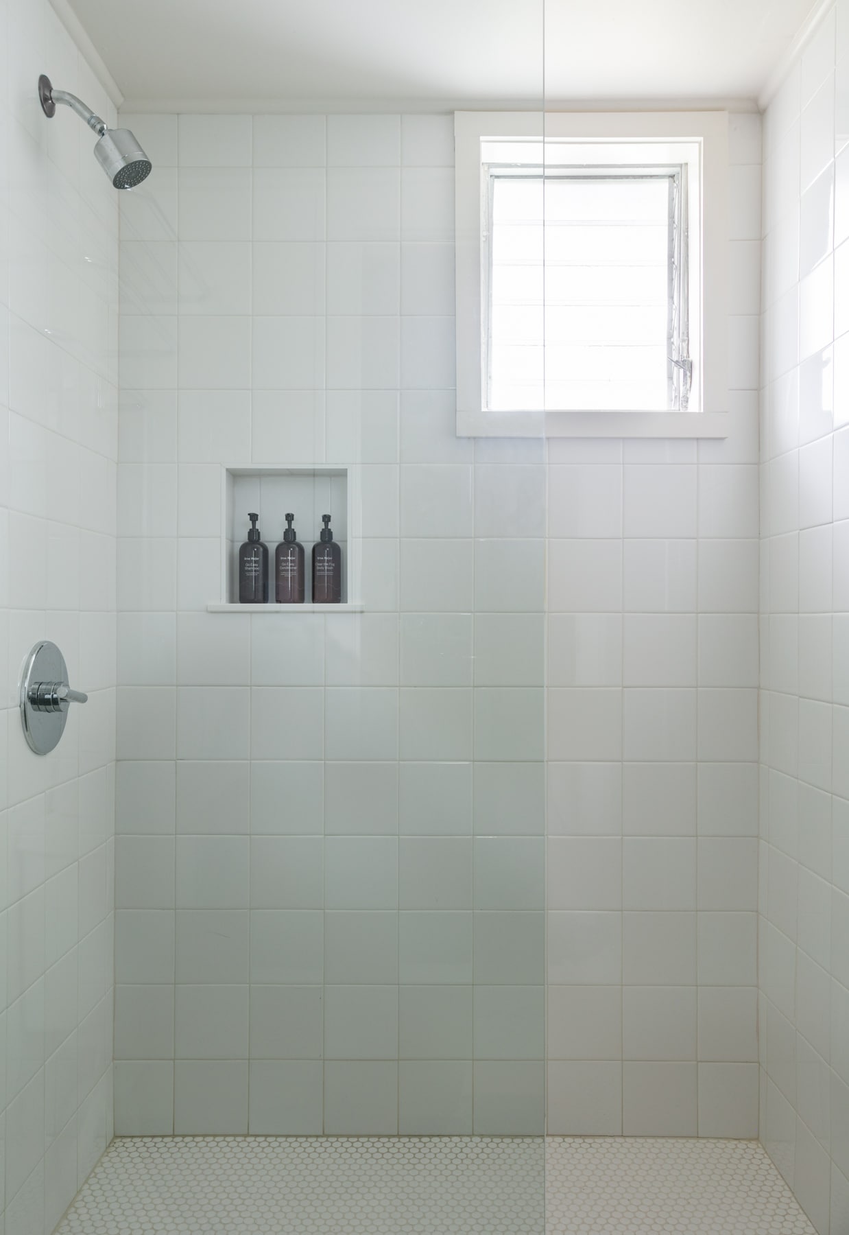 A shower with white tile walls and a niche with three bottles.