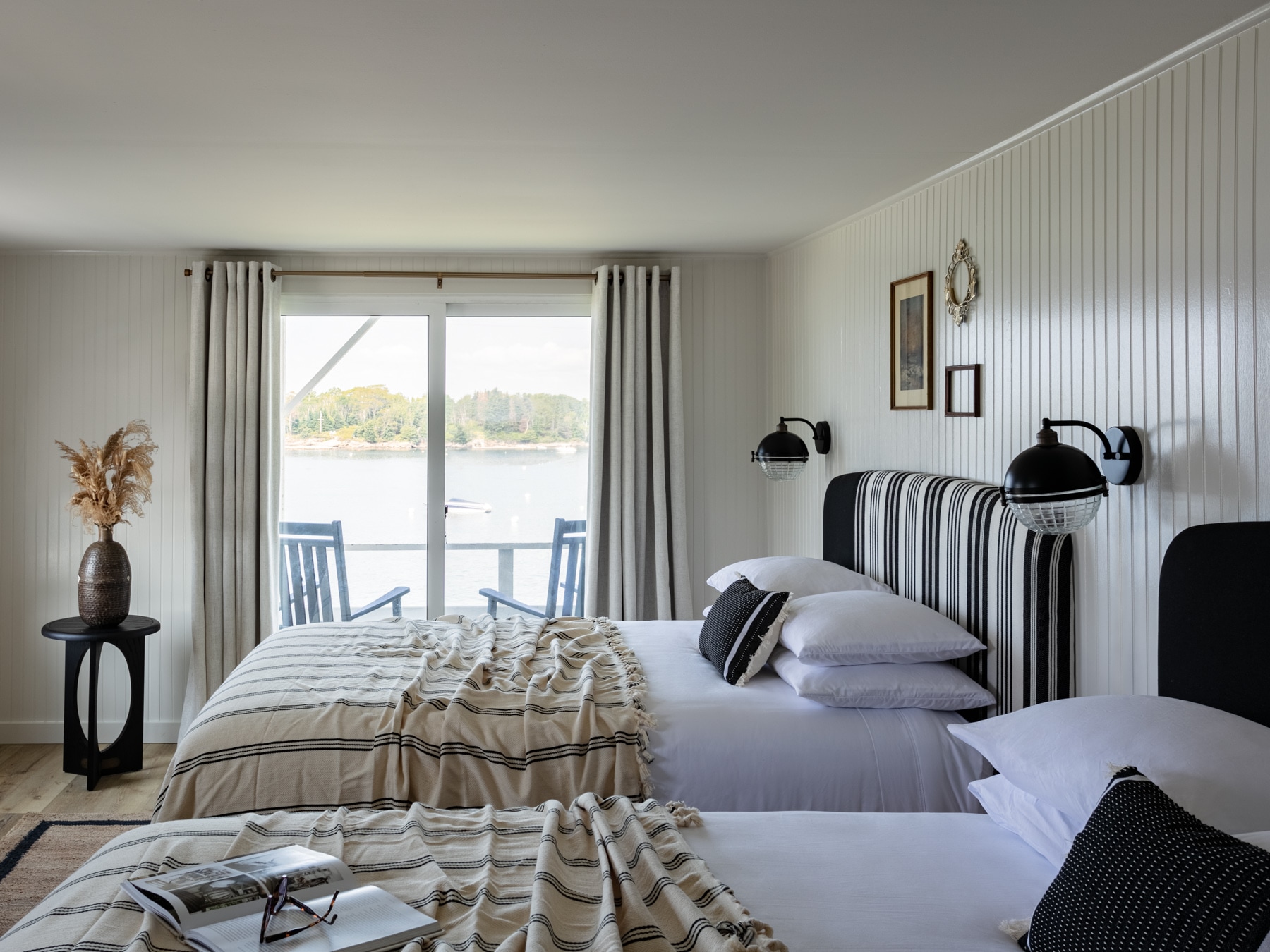 A neatly made bed with a striped headboard and a view of the water through a sliding glass door.