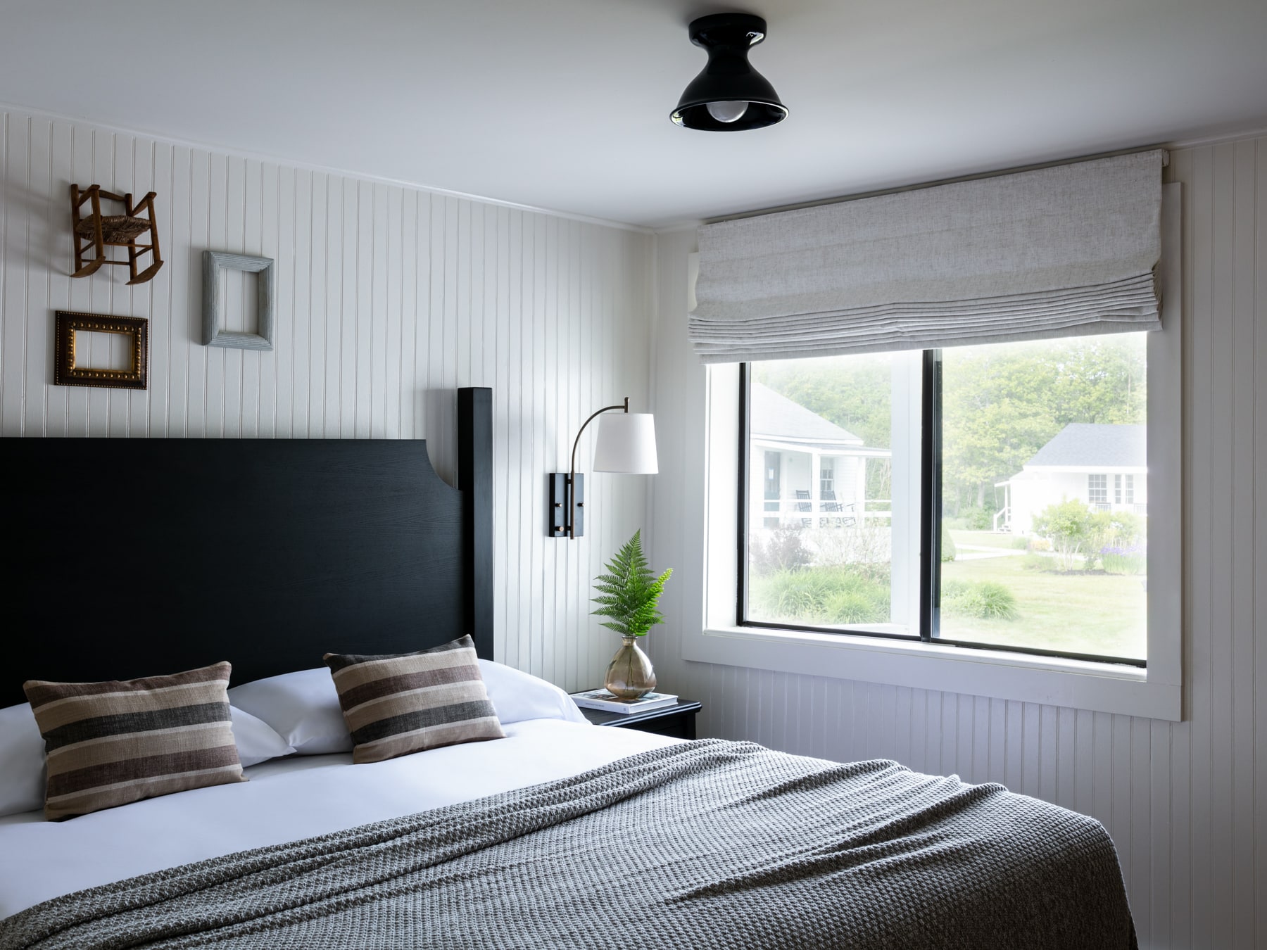 A wide view of a guest room with a bed, window, lamp, and plant.