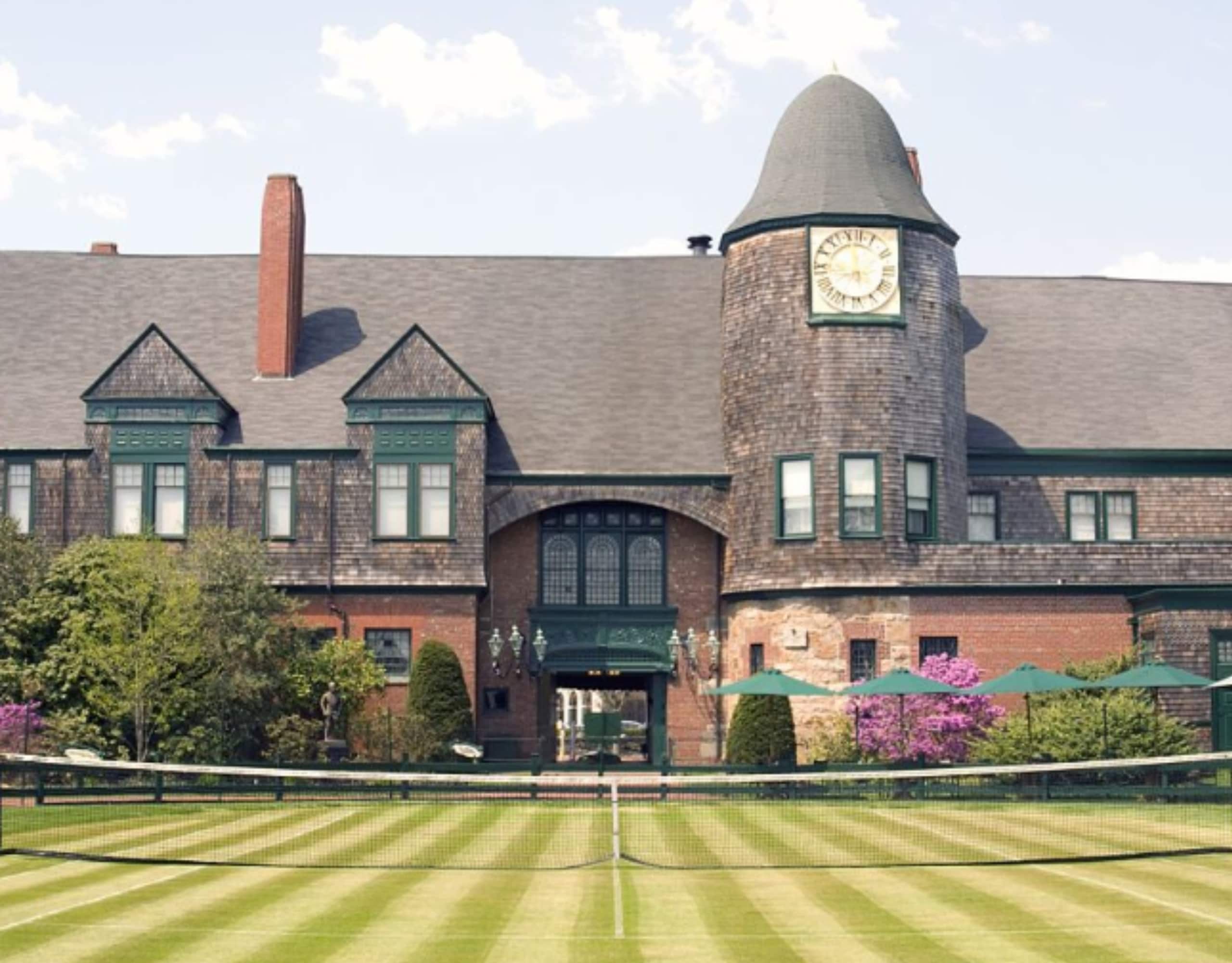 A large brick building with a clock tower and a tennis court in front of it.