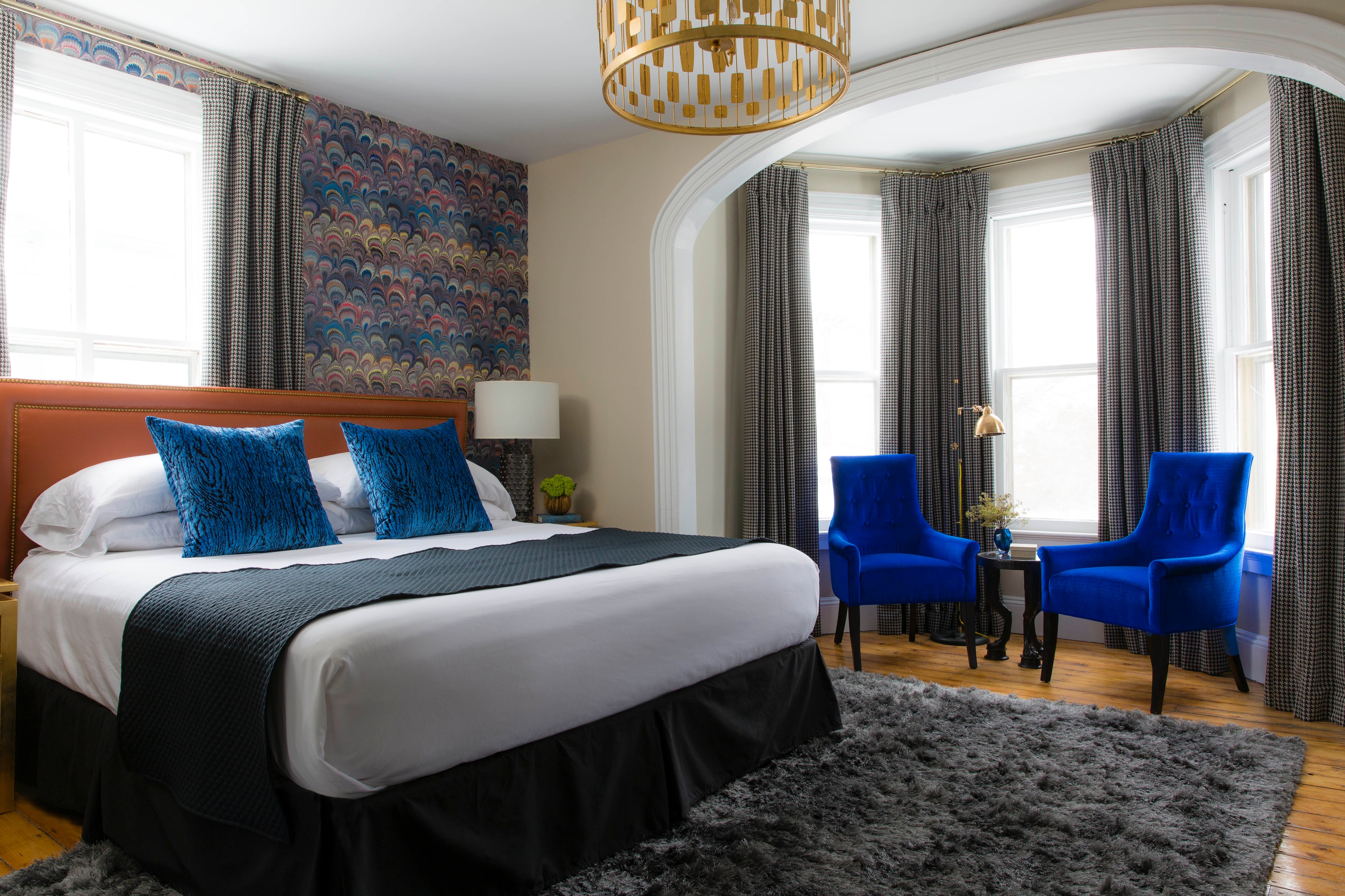 A hotel room with a bed, two blue chairs, and a colorful wall art