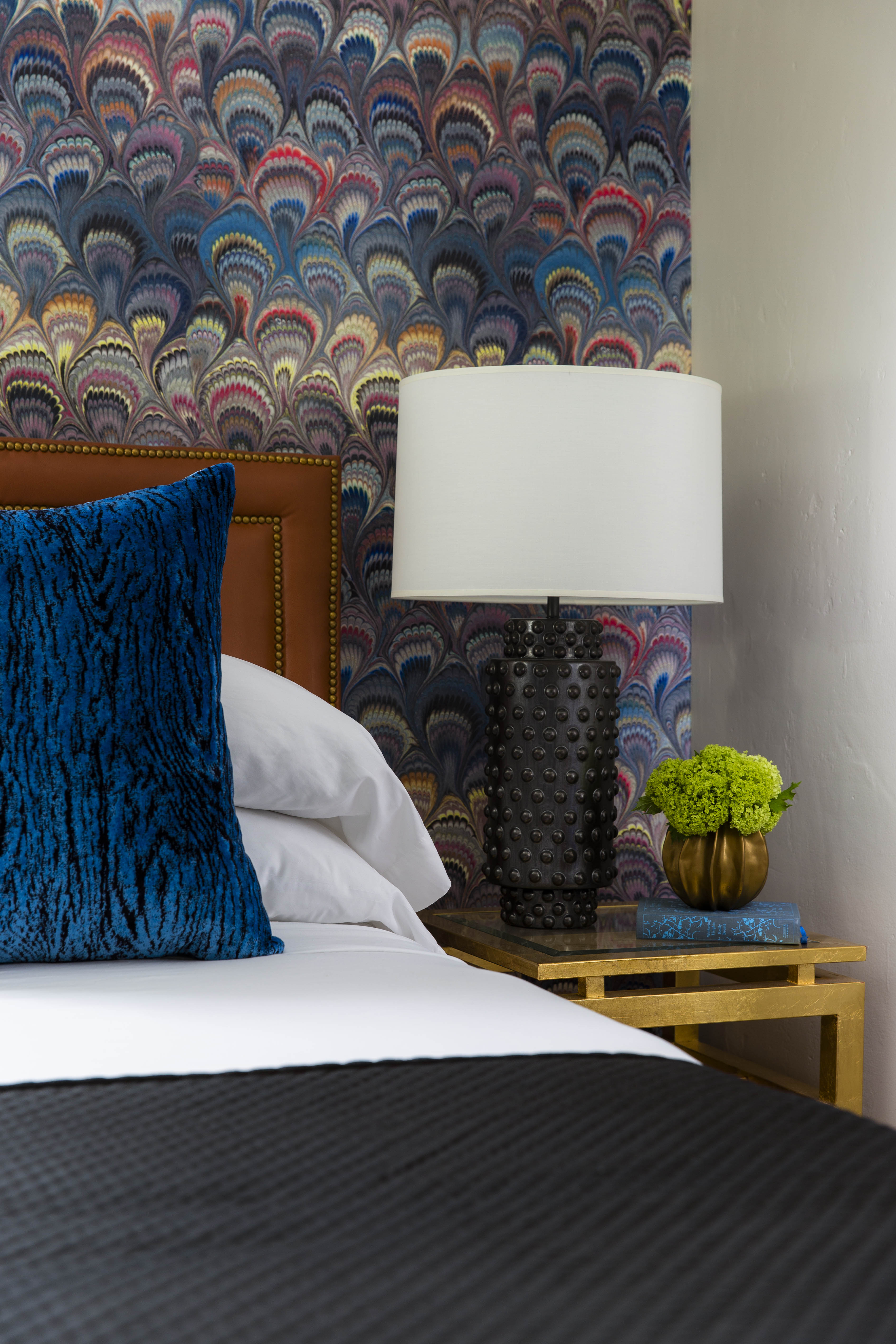 A close-up of a bed with a blue pillow, a lamp, and a nightstand.