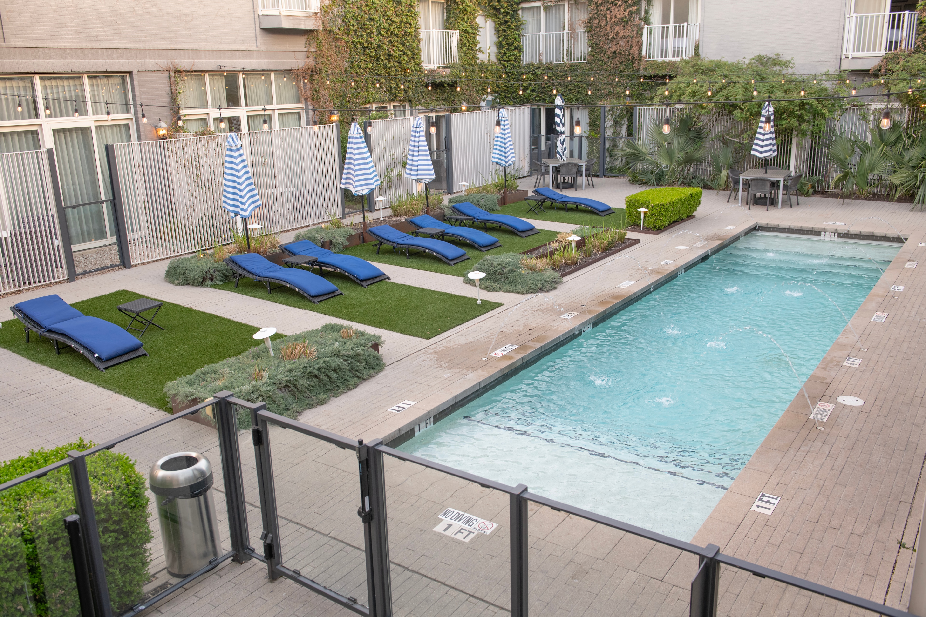 A rectangular pool with blue lounge chairs and striped umbrellas in a paved and grassed area.