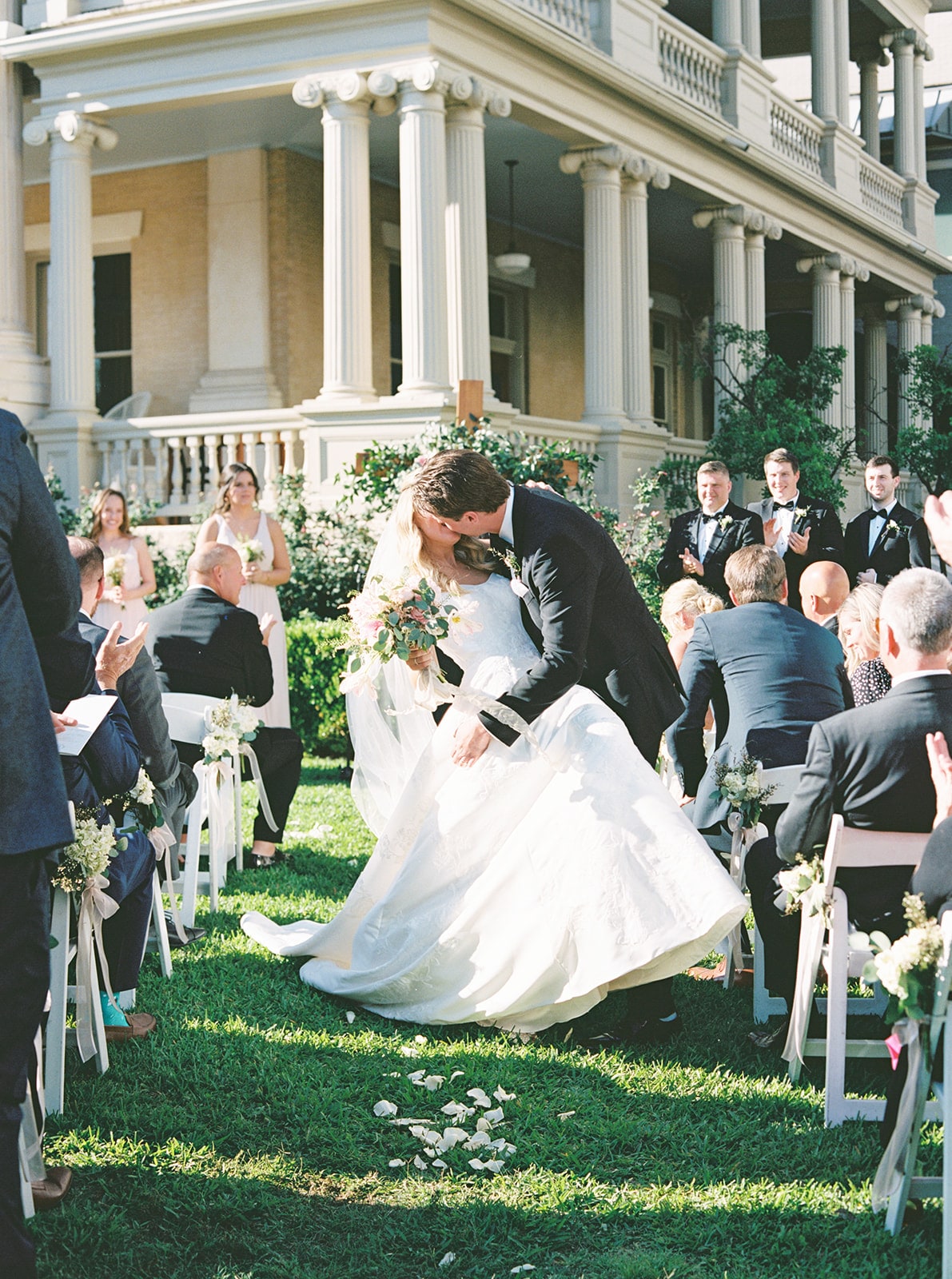 A wedding ceremony on a lawn in front of a large building with columns.