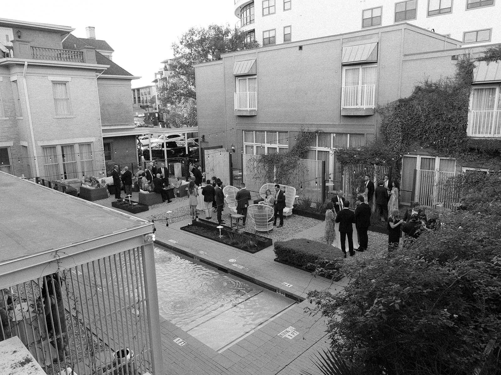 Black and white photo of a courtyard with a pool, people, and buildings