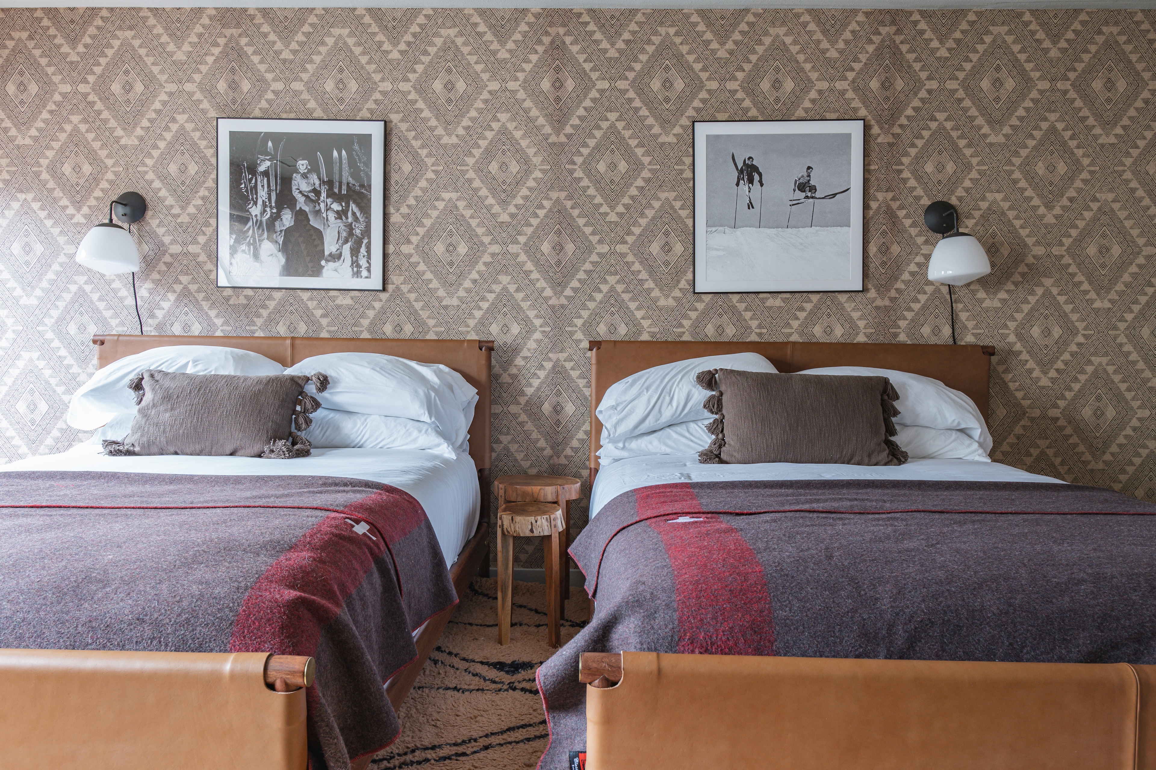A hotel room with two twin beds, wood headboards, and framed ski-themed photos on the wall.