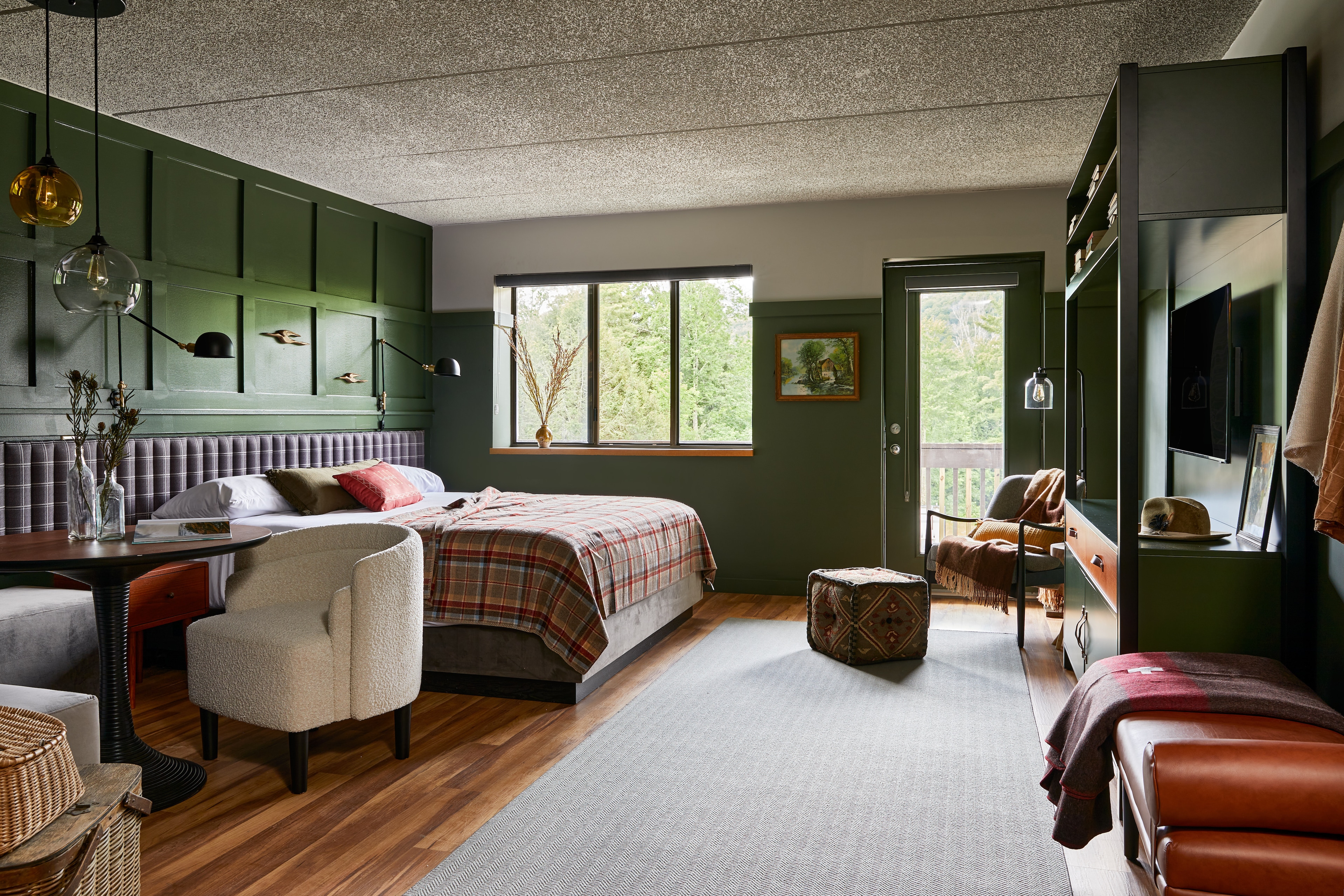 A wide view of a room with a plaid bedspread, green walls, and wood floors.