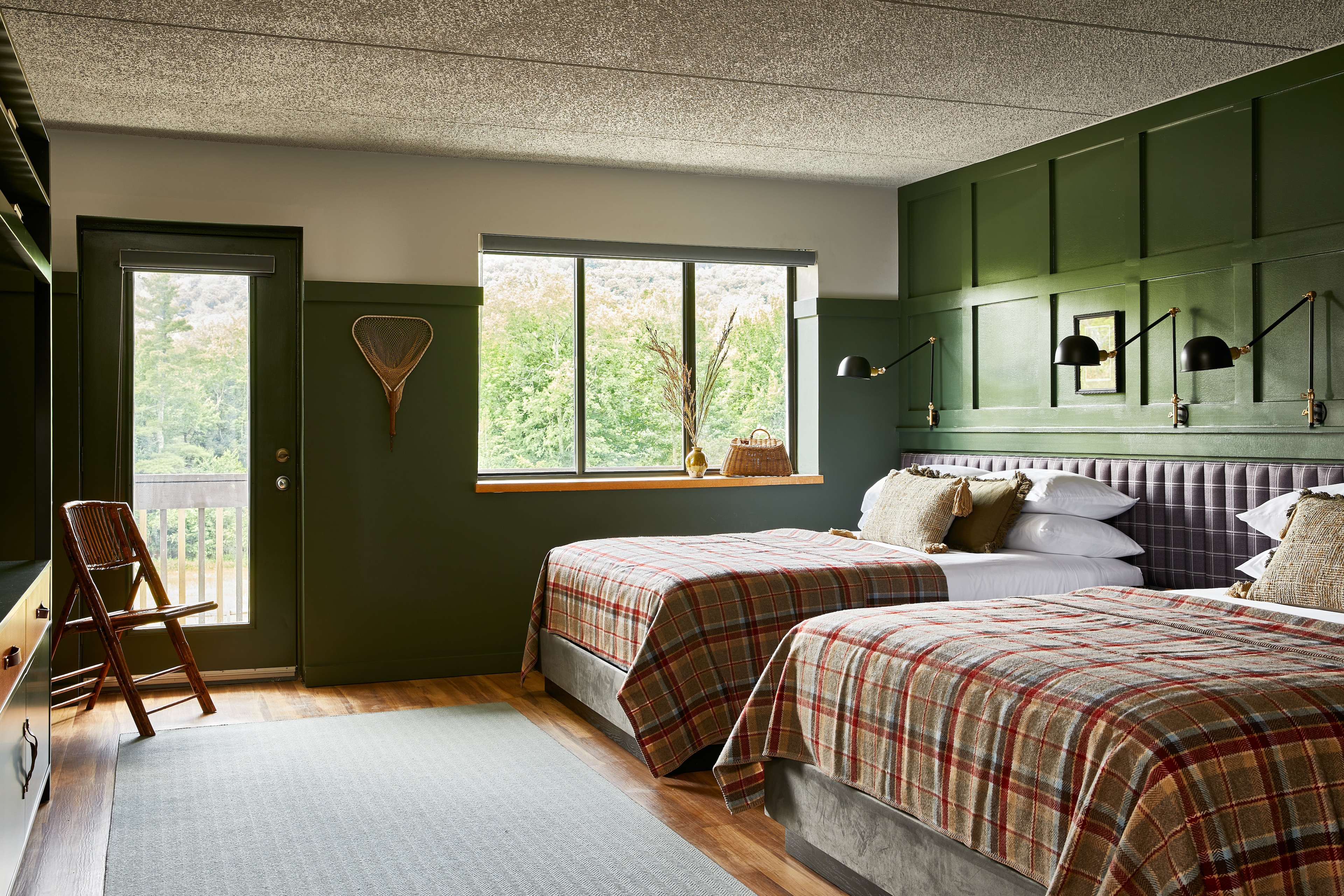 A cozy room with two beds, green walls, and a window showing trees outside.