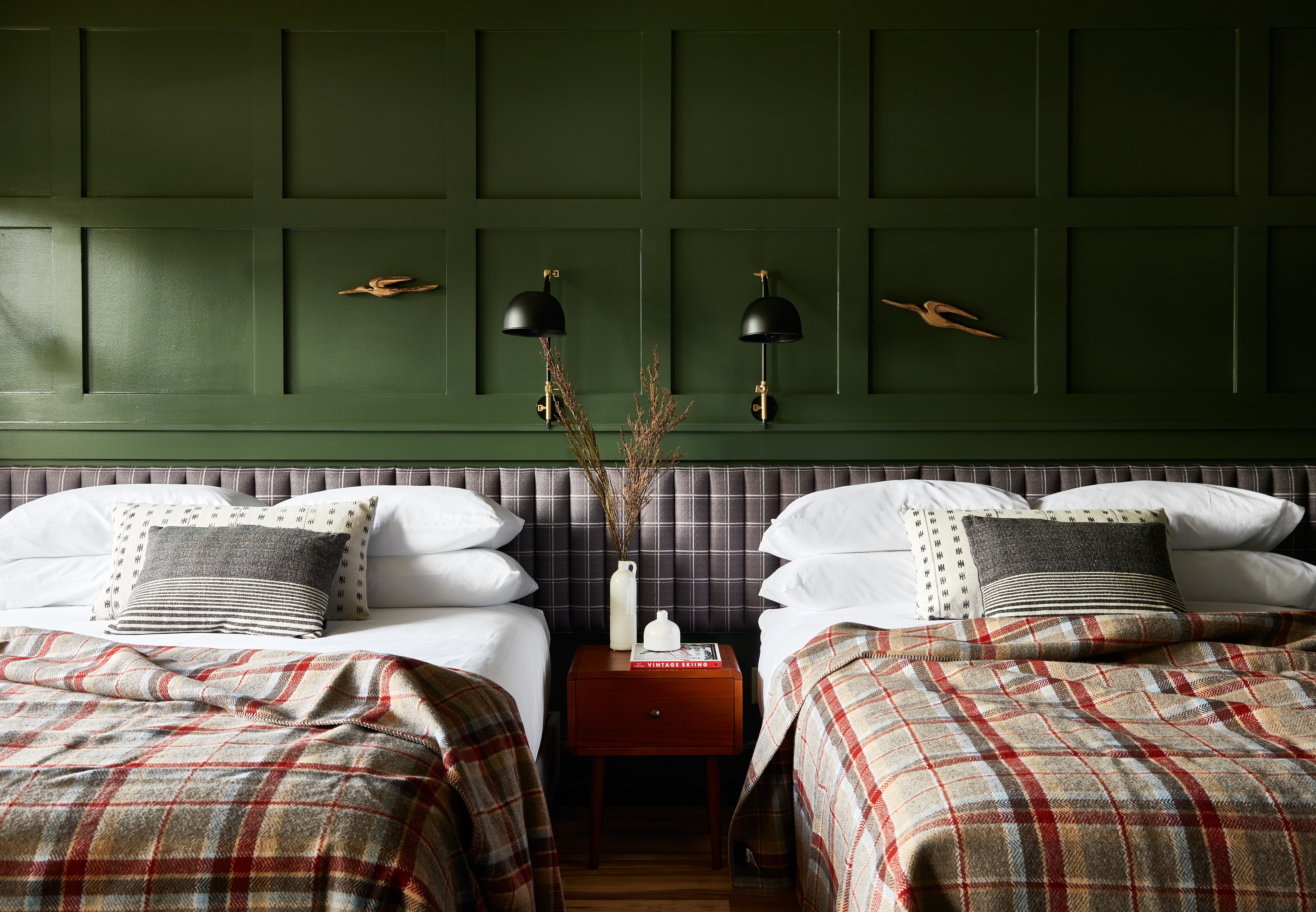 A hotel room with two beds, a wooden nightstand, and a plaid headboard.