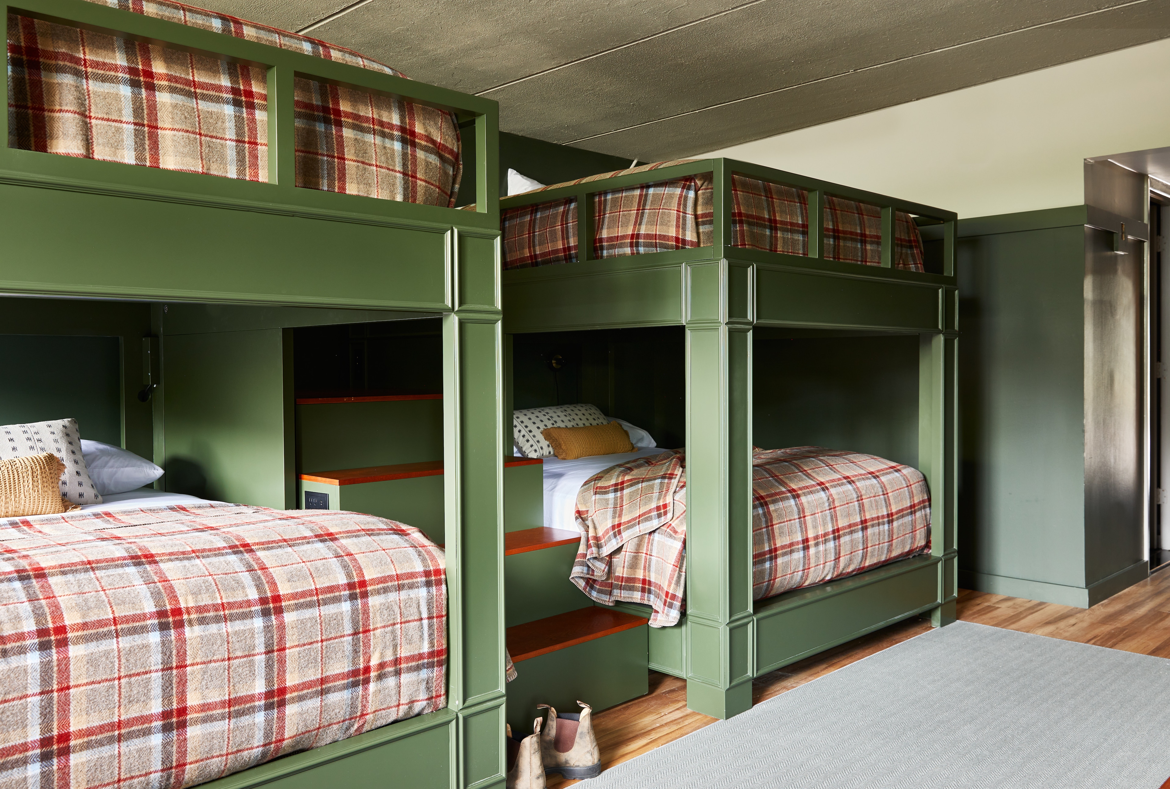 A room with green walls and bunk beds with plaid bedding.