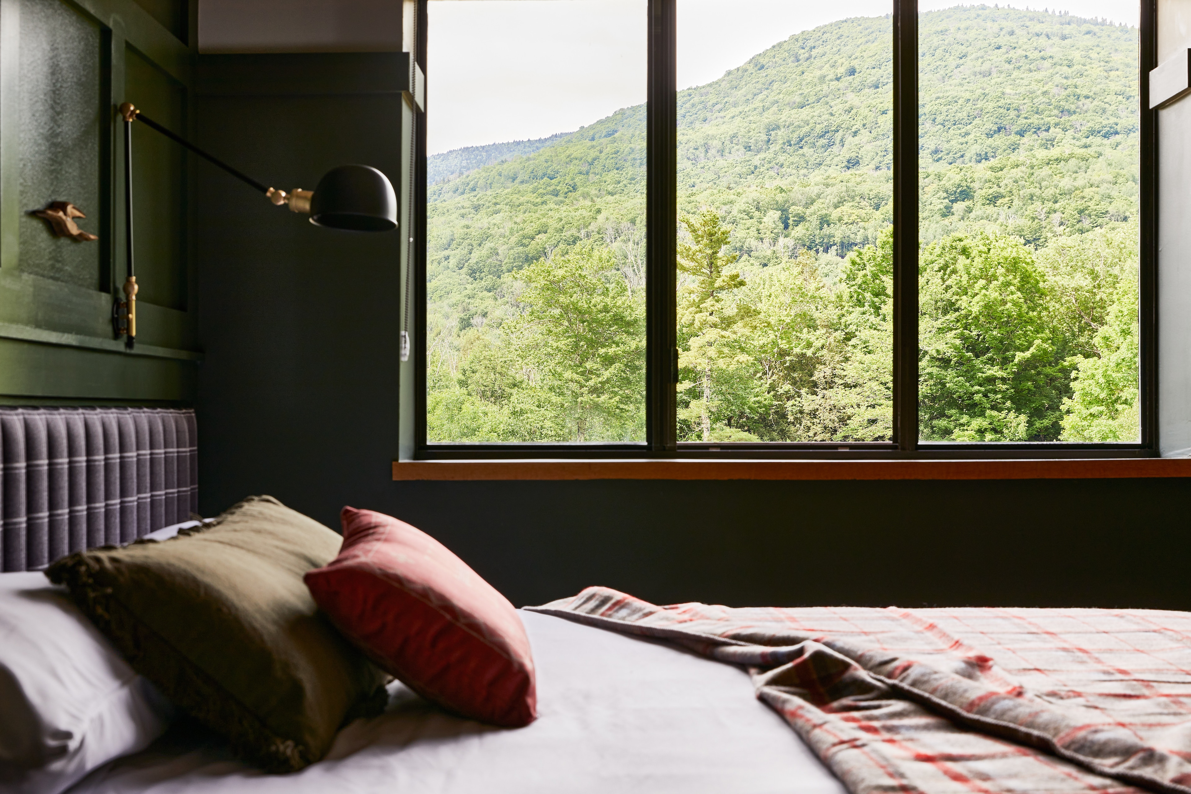 a bed with pillows in front of a large window with a view of green mountains