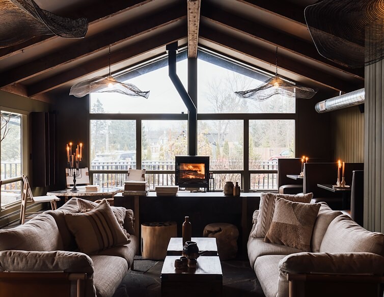 The Lodge at AWOL Stowe, with a lit fireplace and large windows overlooking the forest