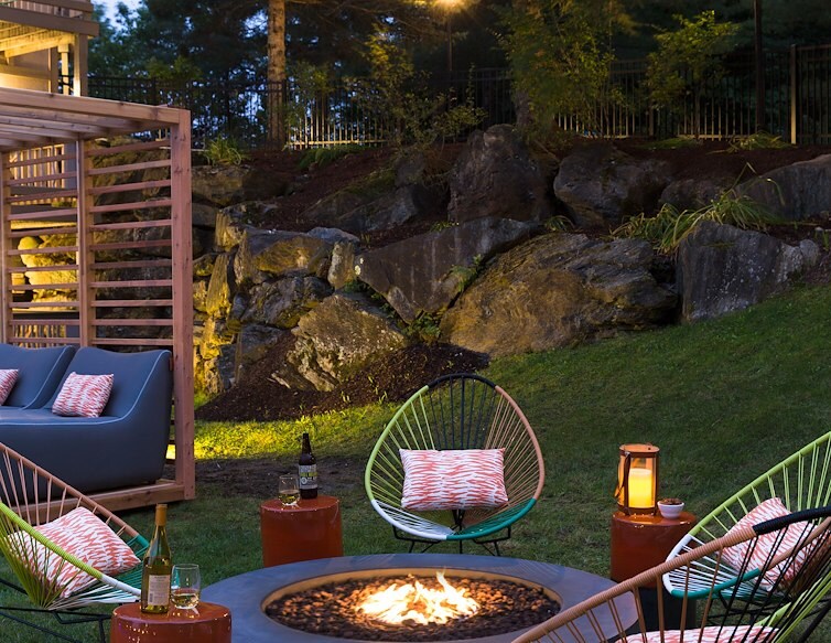 A fire pit with chairs and a pergola in the back