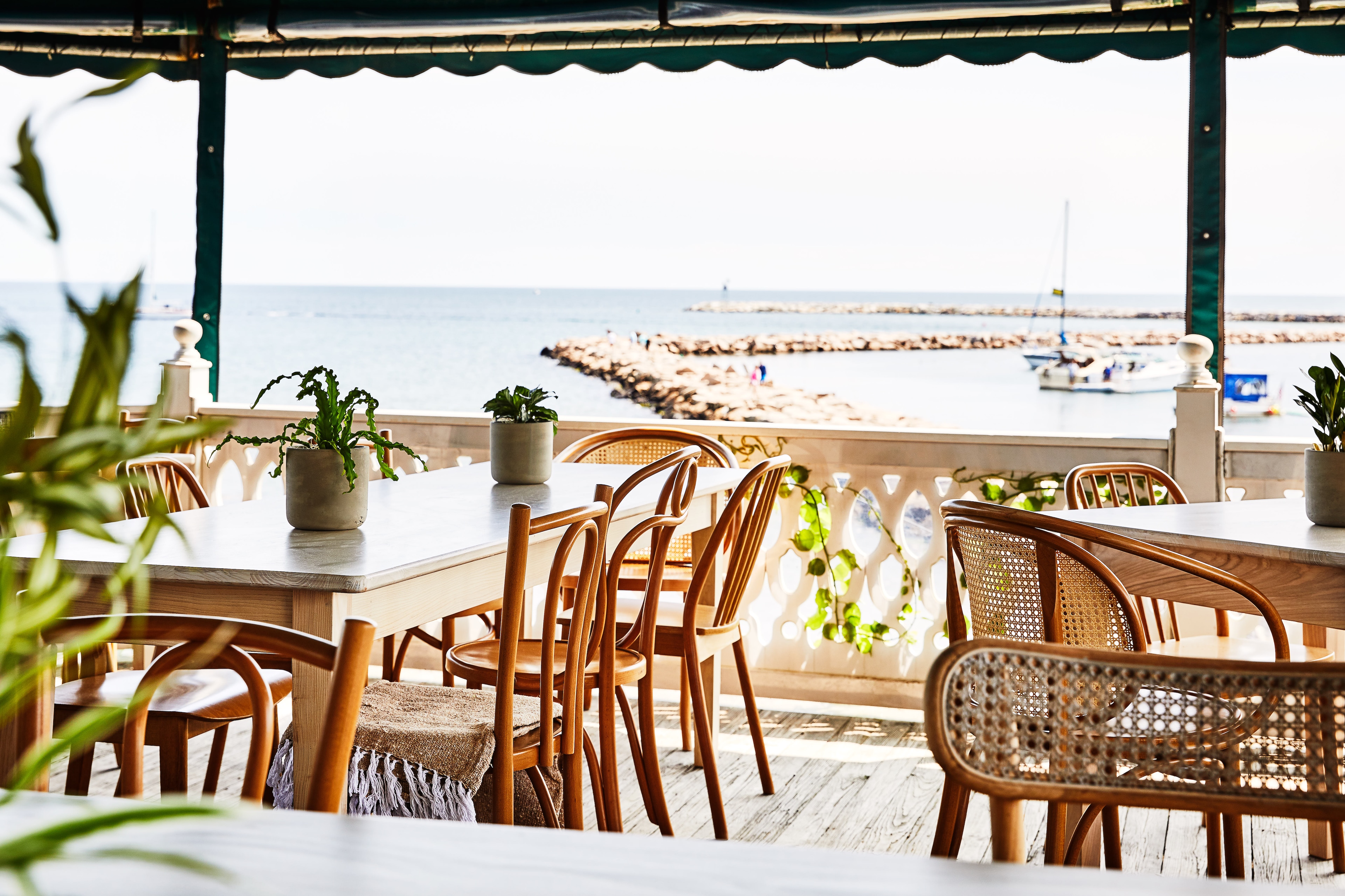 An outdoor dining area with wooden chairs and white tables overlooking the ocean.