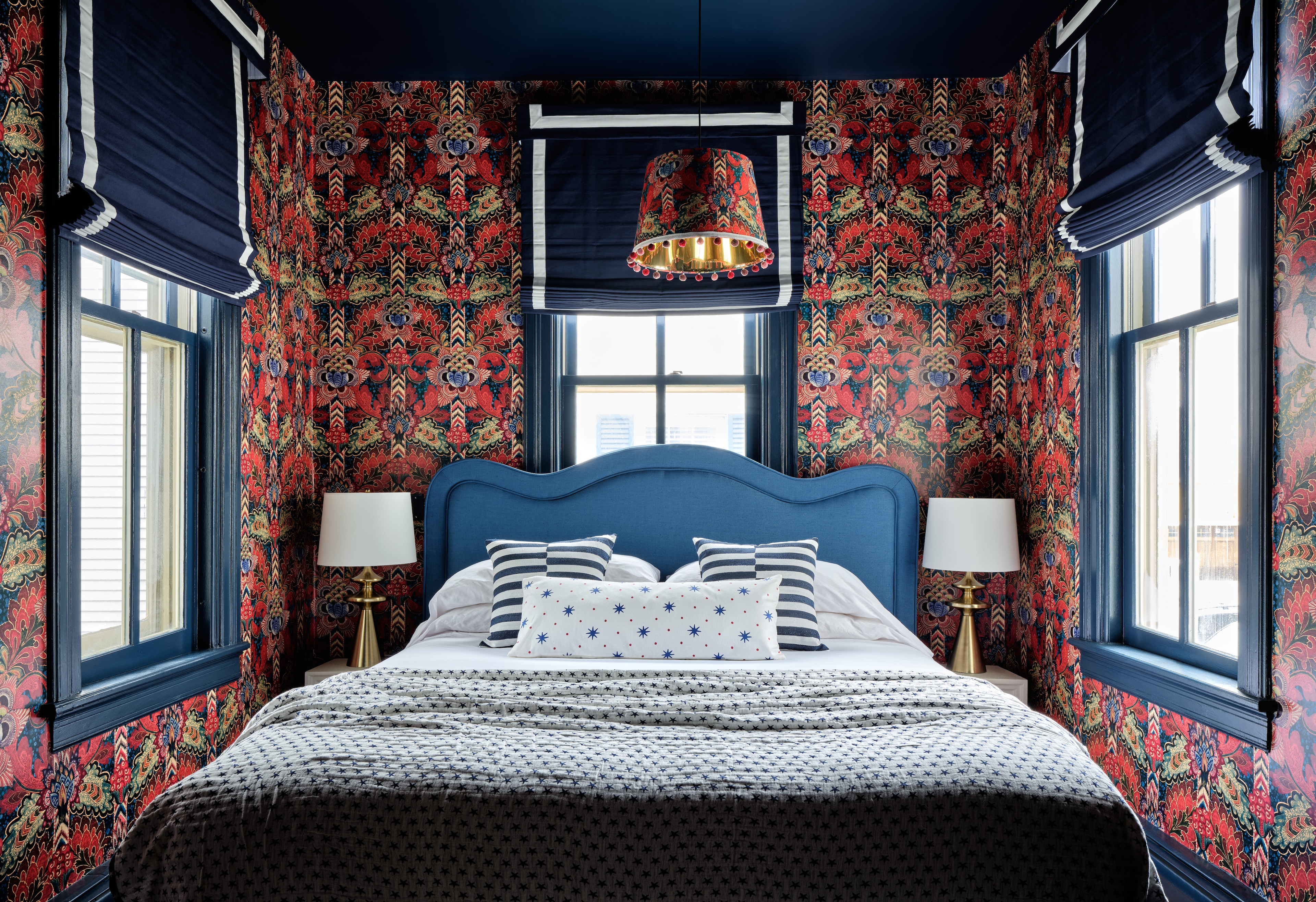 A bed with a blue headboard and floral wallpaper in a guest room