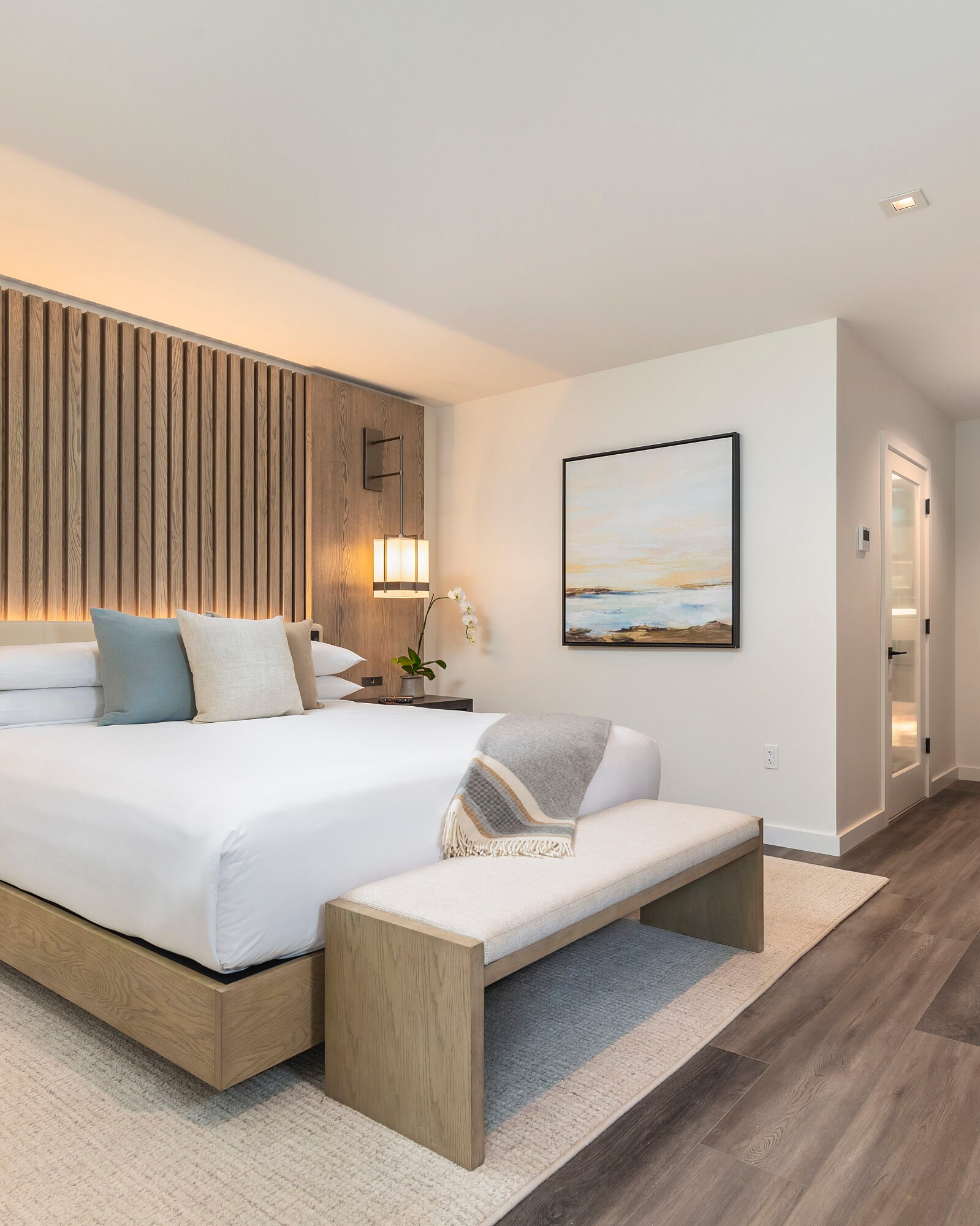 A hotel room with a large bed, bench, and artwork.
