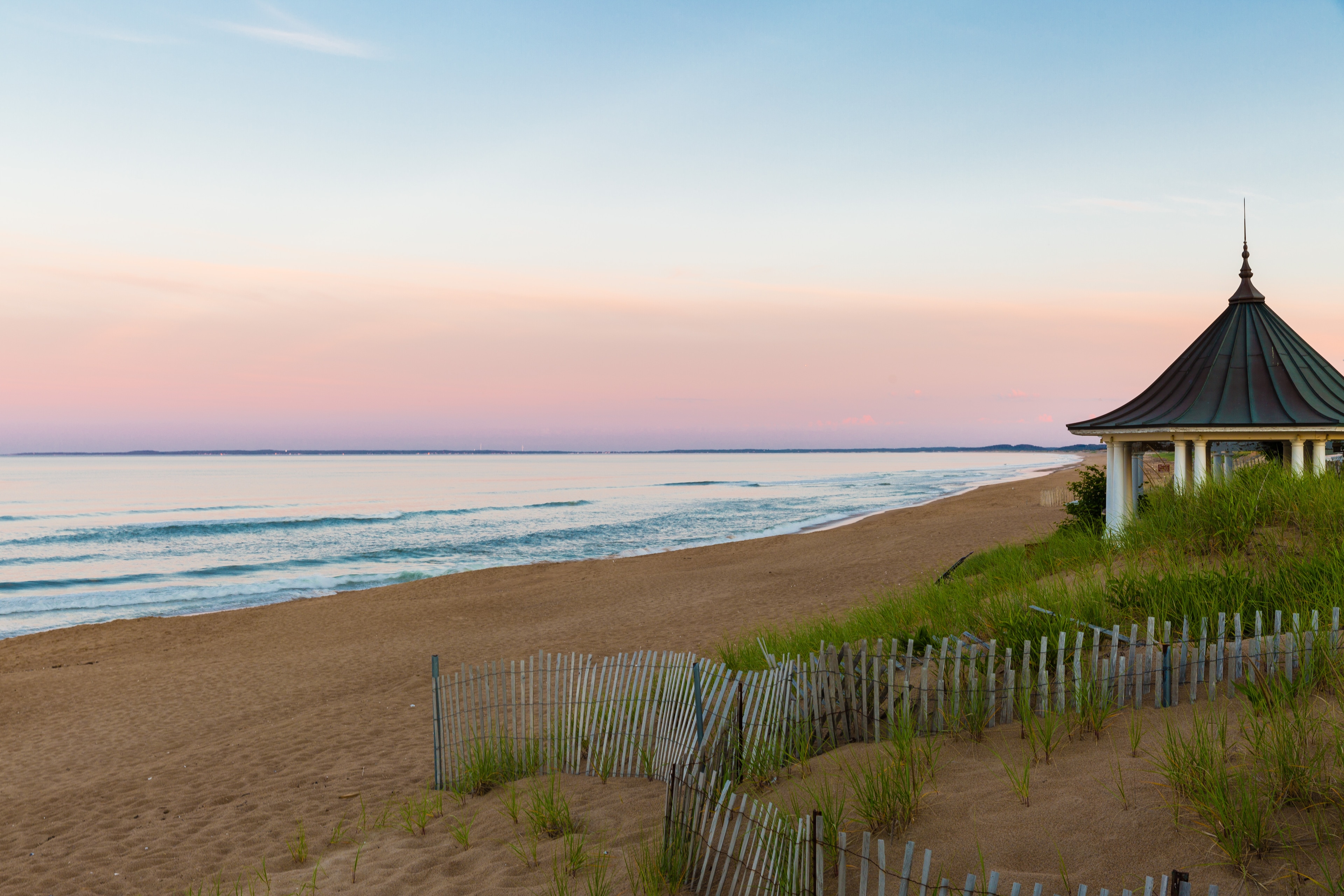 A beach scene with a gazebo on the right side, overlooking the ocean at sunset.