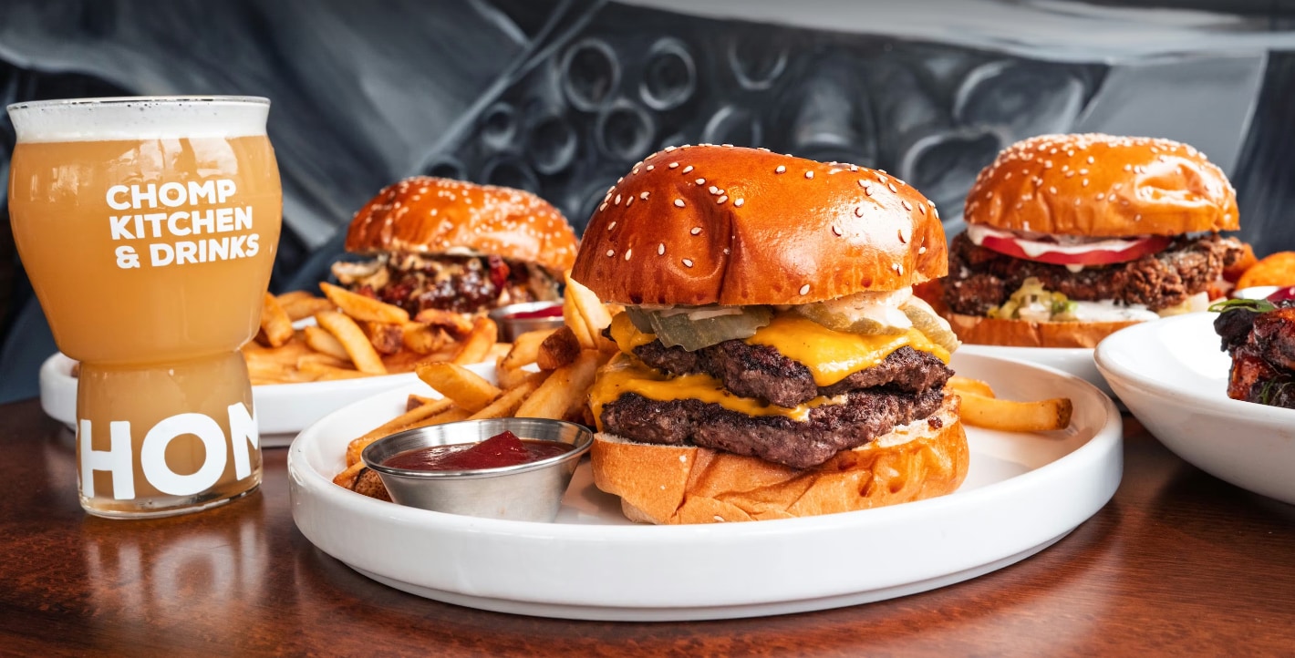 A plate of burgers and fries with a glass of beer on a table.