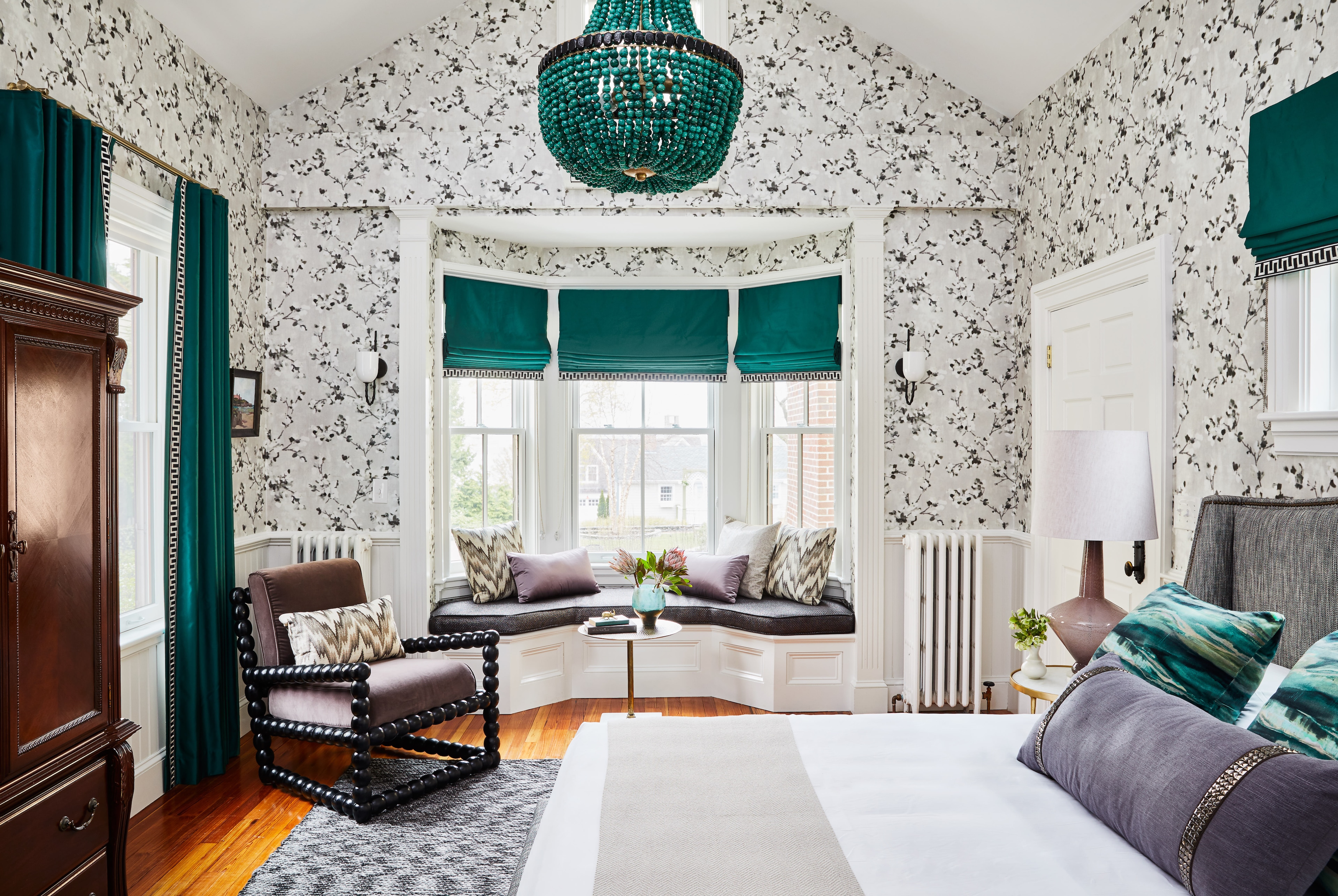 A luxurious guest room with a large bed, window seat, and chandelier.