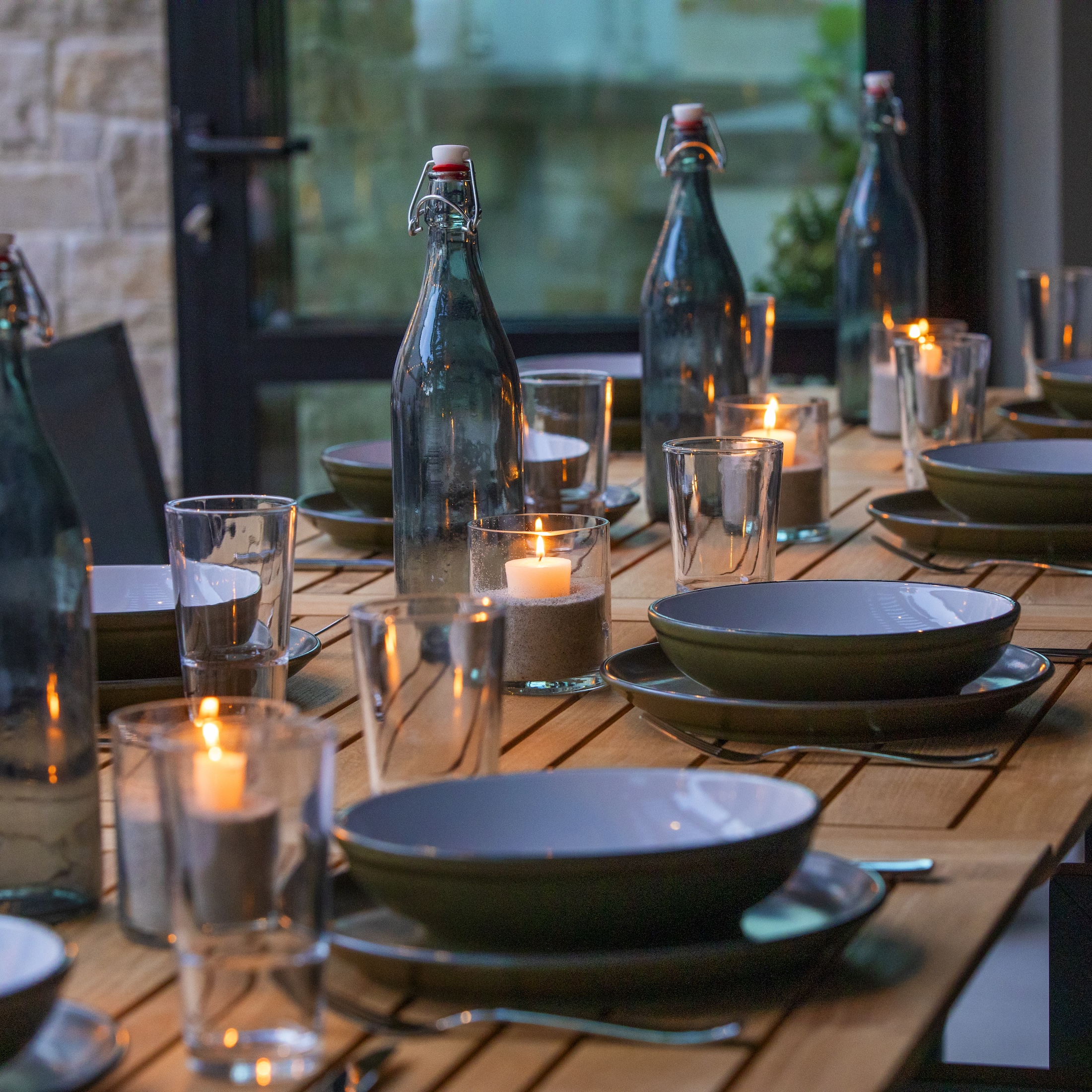 A table set for dinner with lit candles, green bottles, and dinnerware