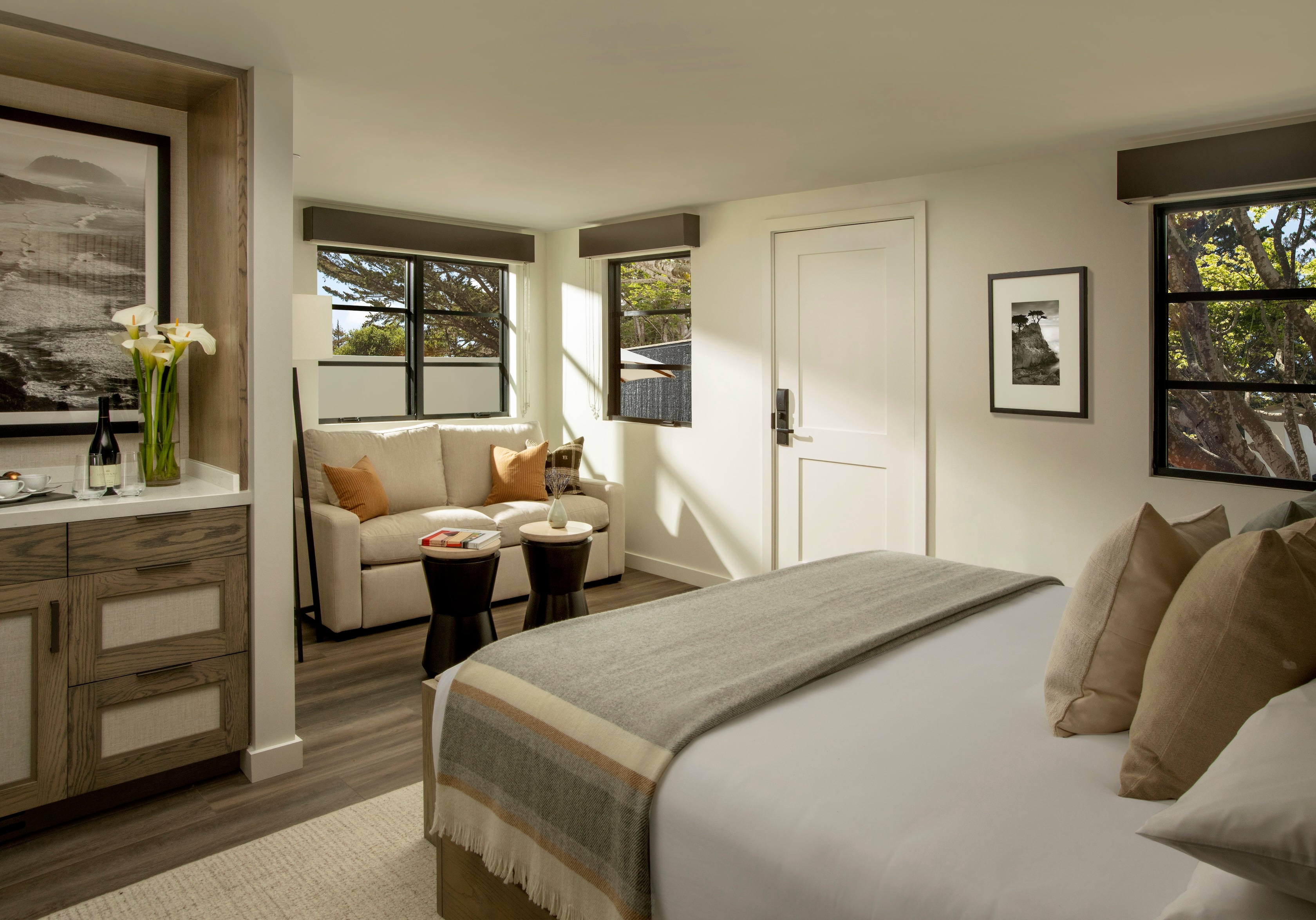 A hotel room with a bed, sitting area, and windows.
