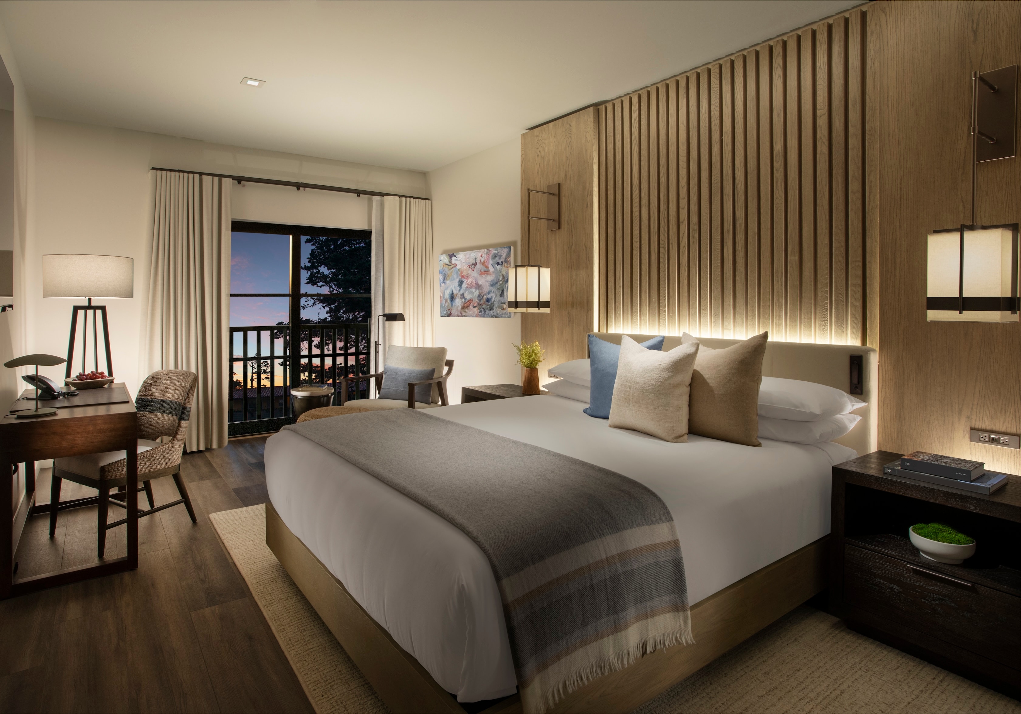 A hotel room with a large bed, desk, chairs, and a balcony with a view.