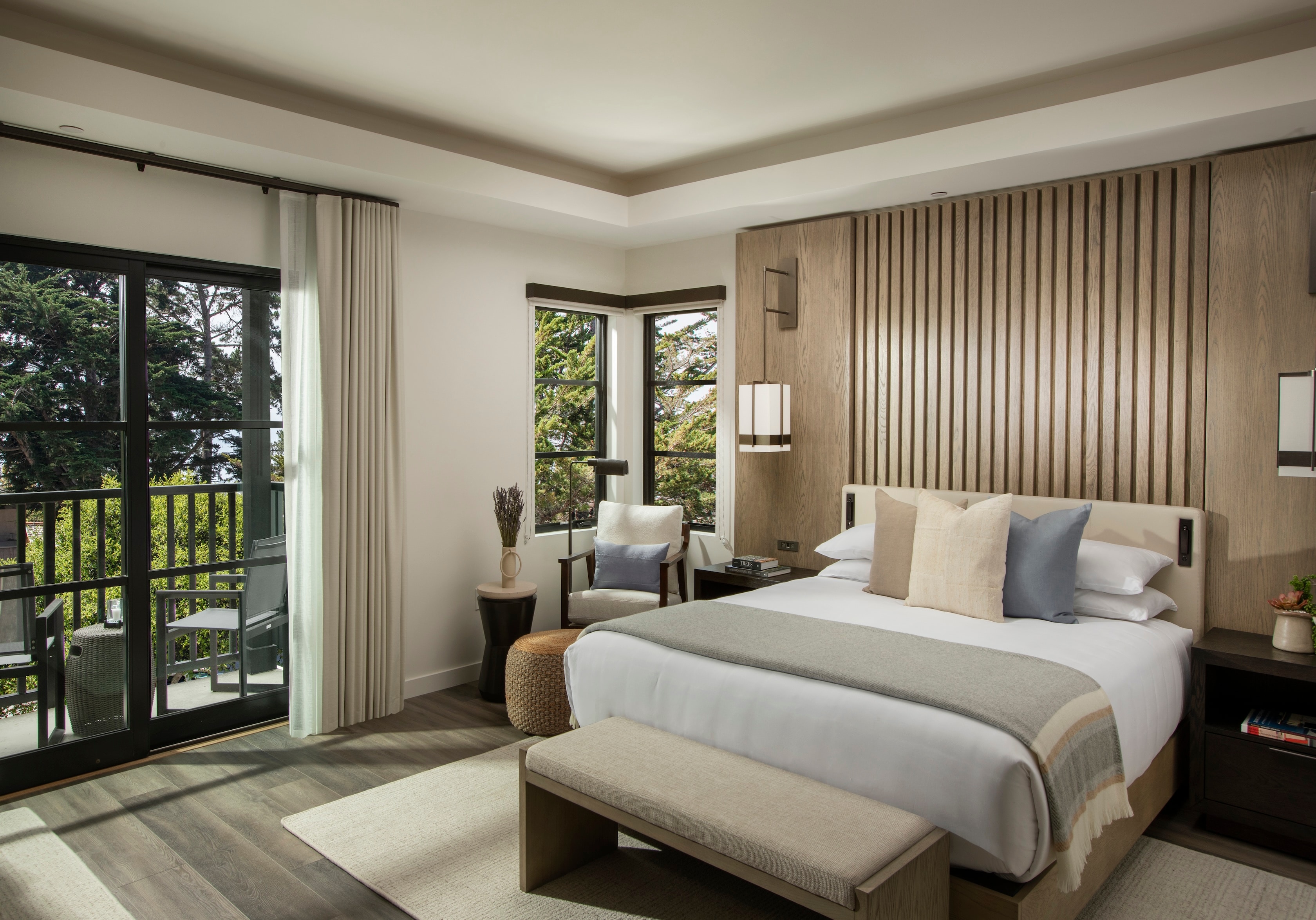 A hotel room with a bed, window, balcony, chair, and nightstand.