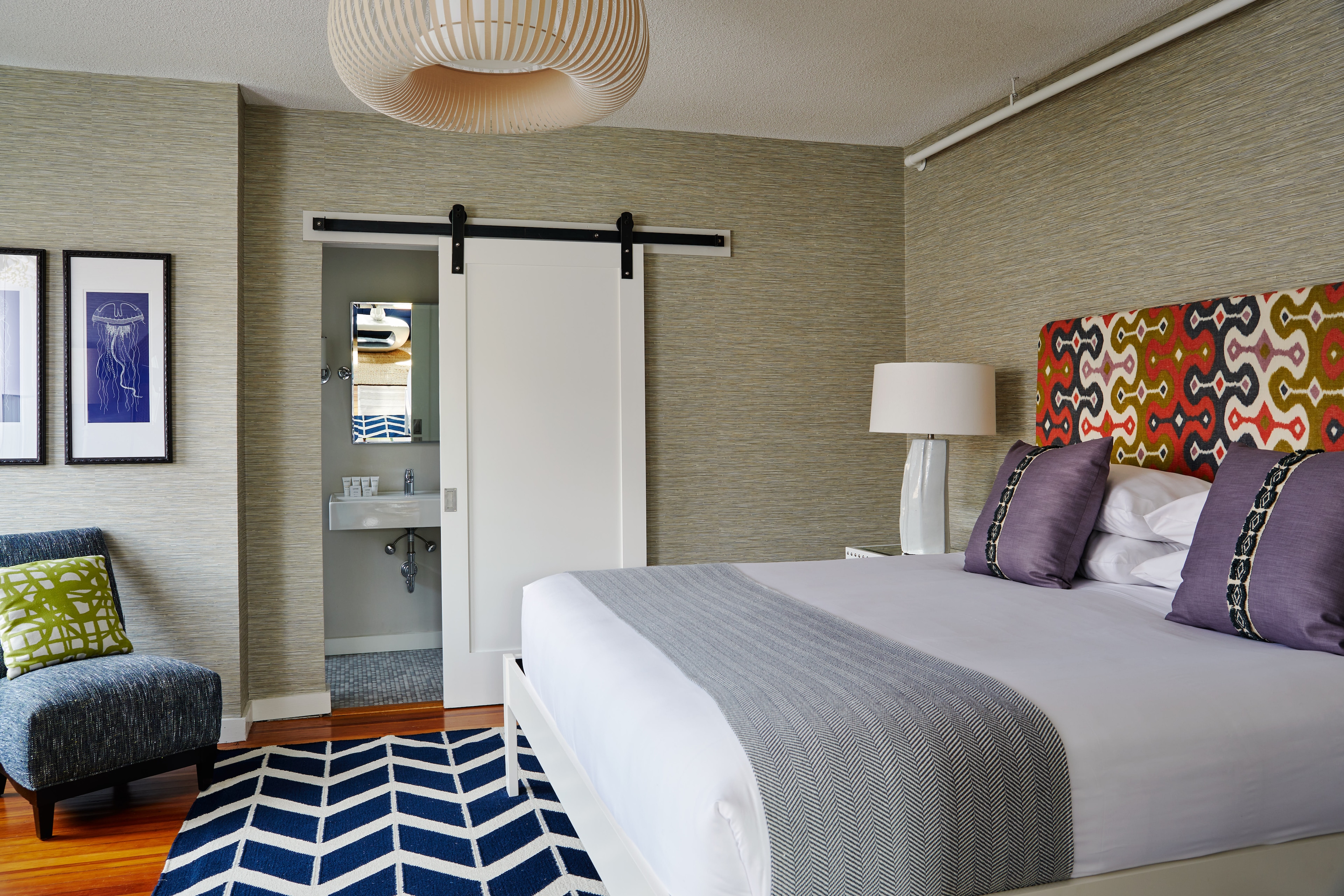 A hotel room with a bed, chair, and bathroom in the background.