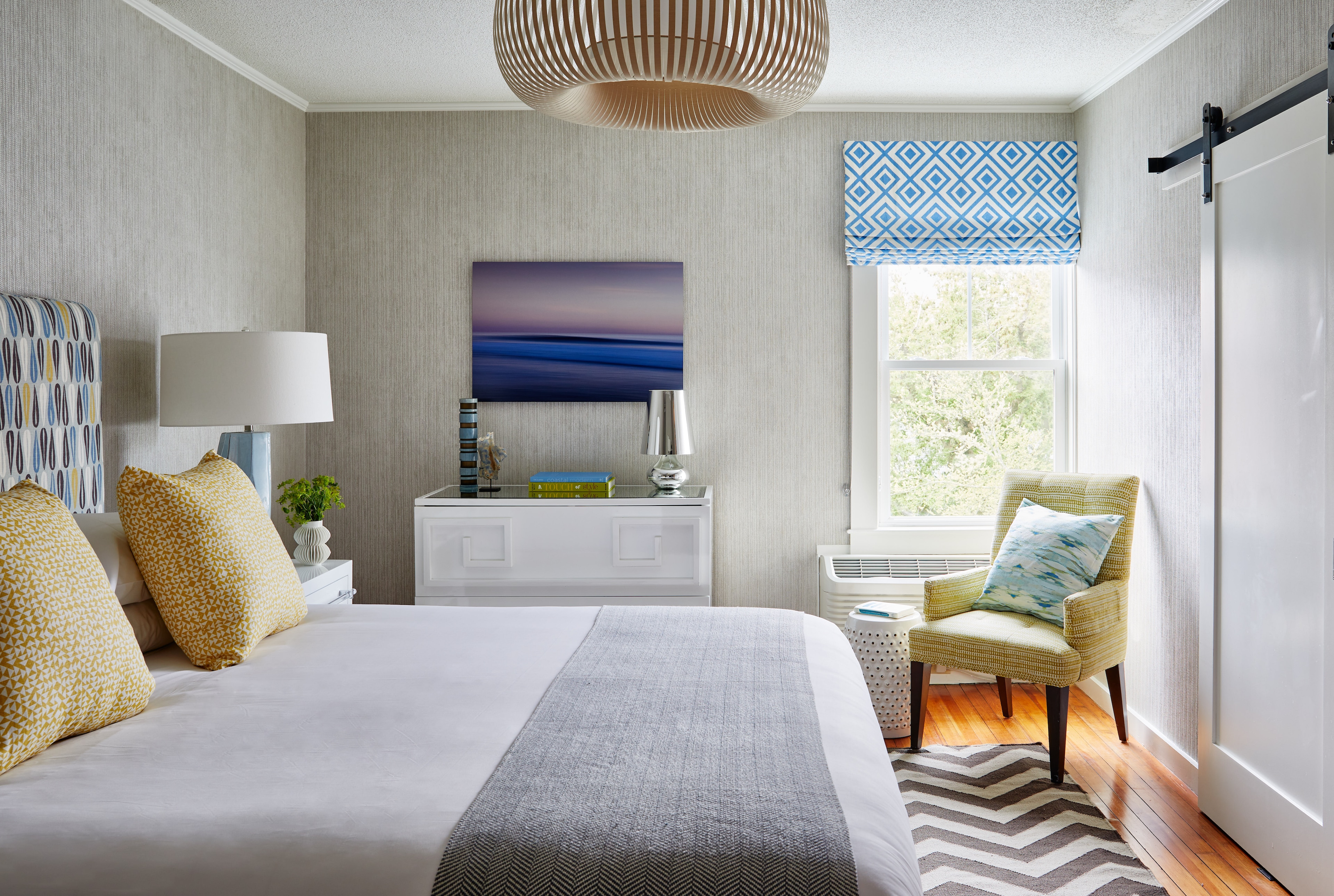 A wide view of a hotel room with a bed, chair, and window