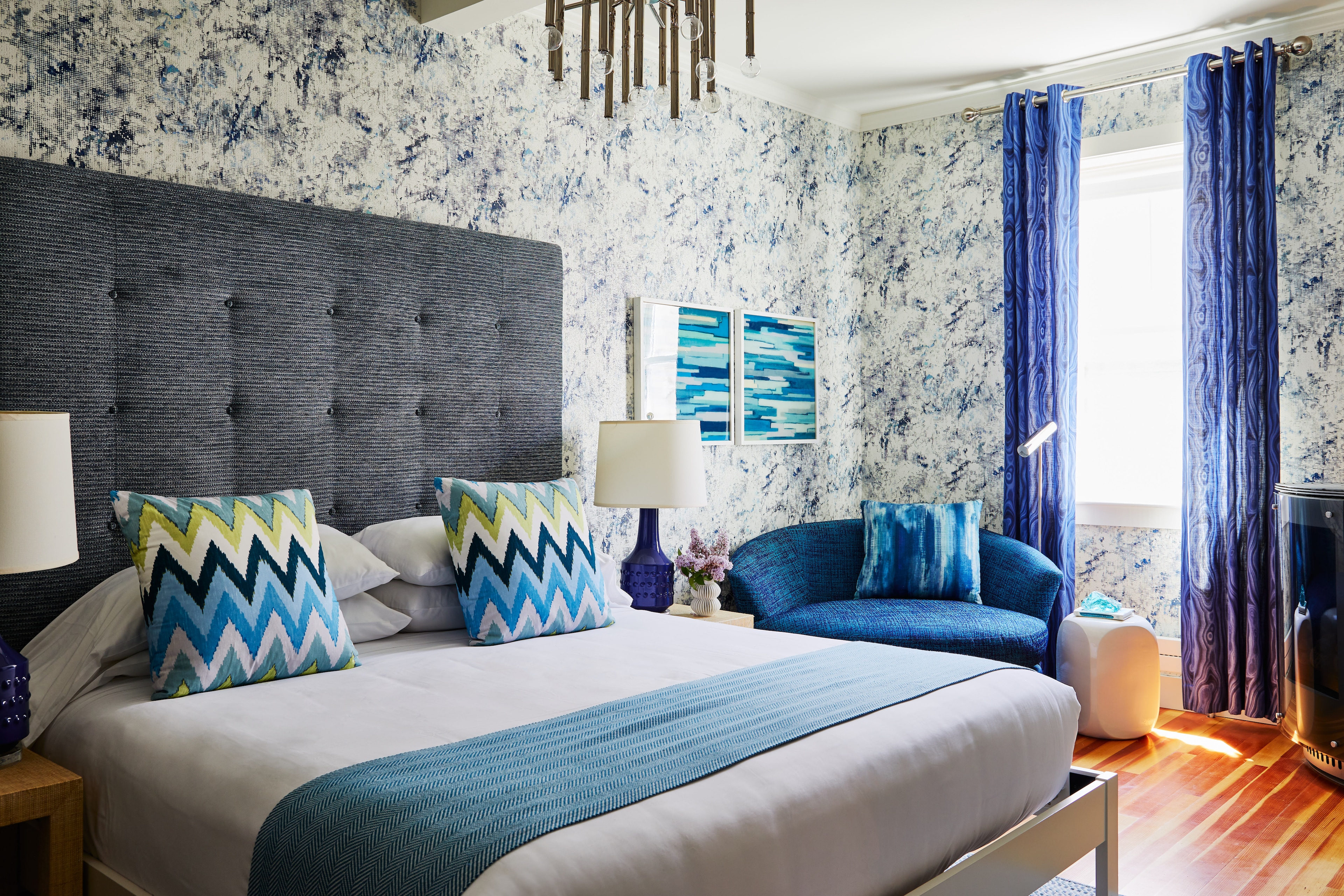 A neatly made bed with a blue and white color scheme and a patterned wallpaper in a hotel room.