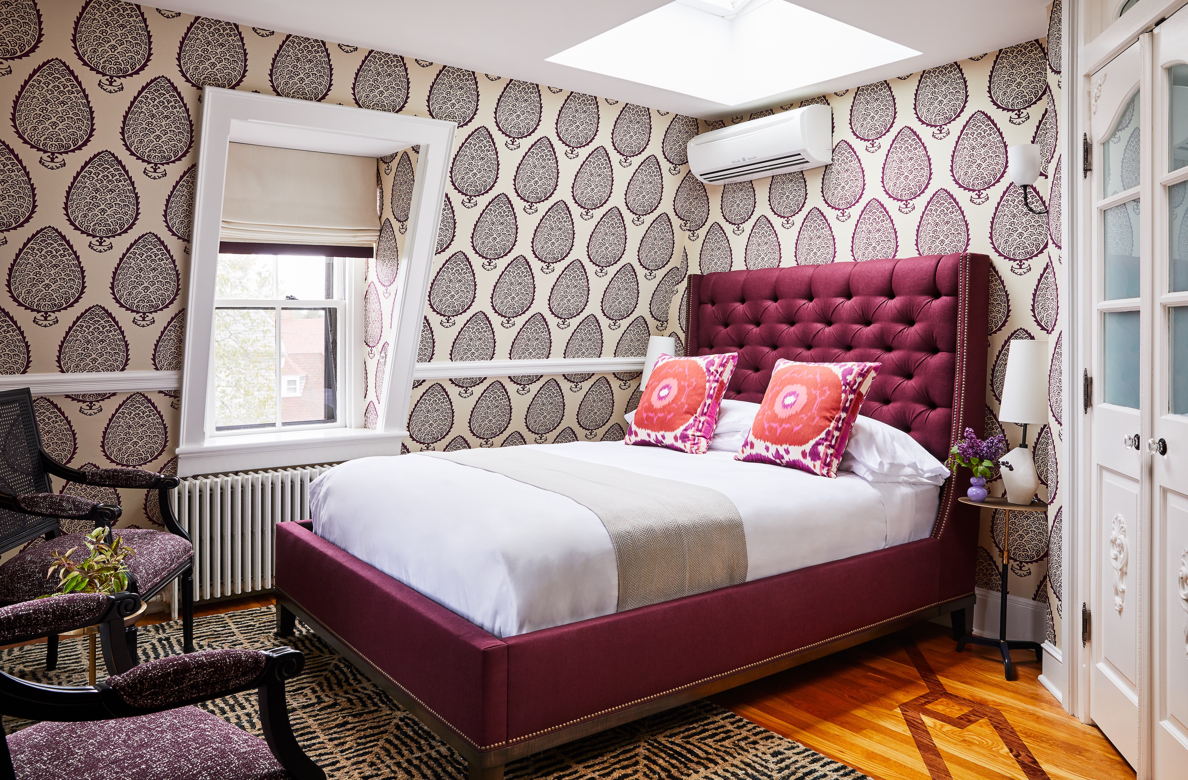 A neatly made bed with a tufted headboard and patterned wallpaper in a guest room.