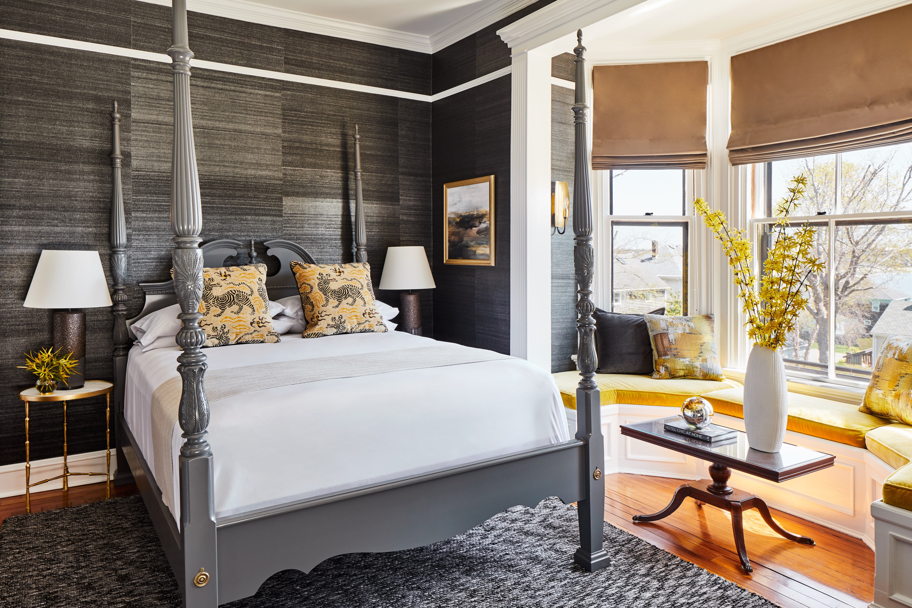 A stylish hotel room with a four-poster bed, window seat, and modern furnishings.