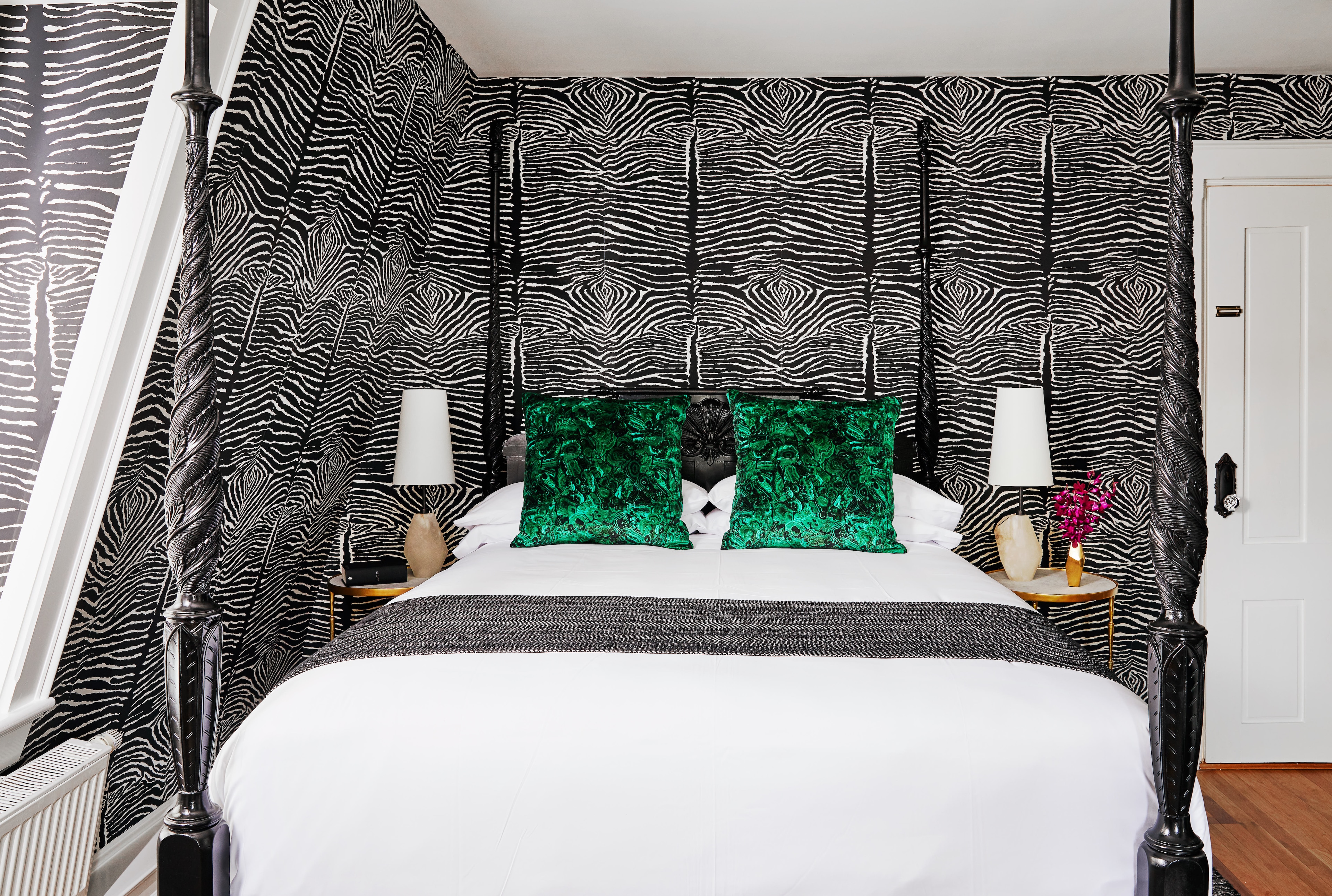 A bed with white bedding and green pillows against a black and white zebra print wallpaper.