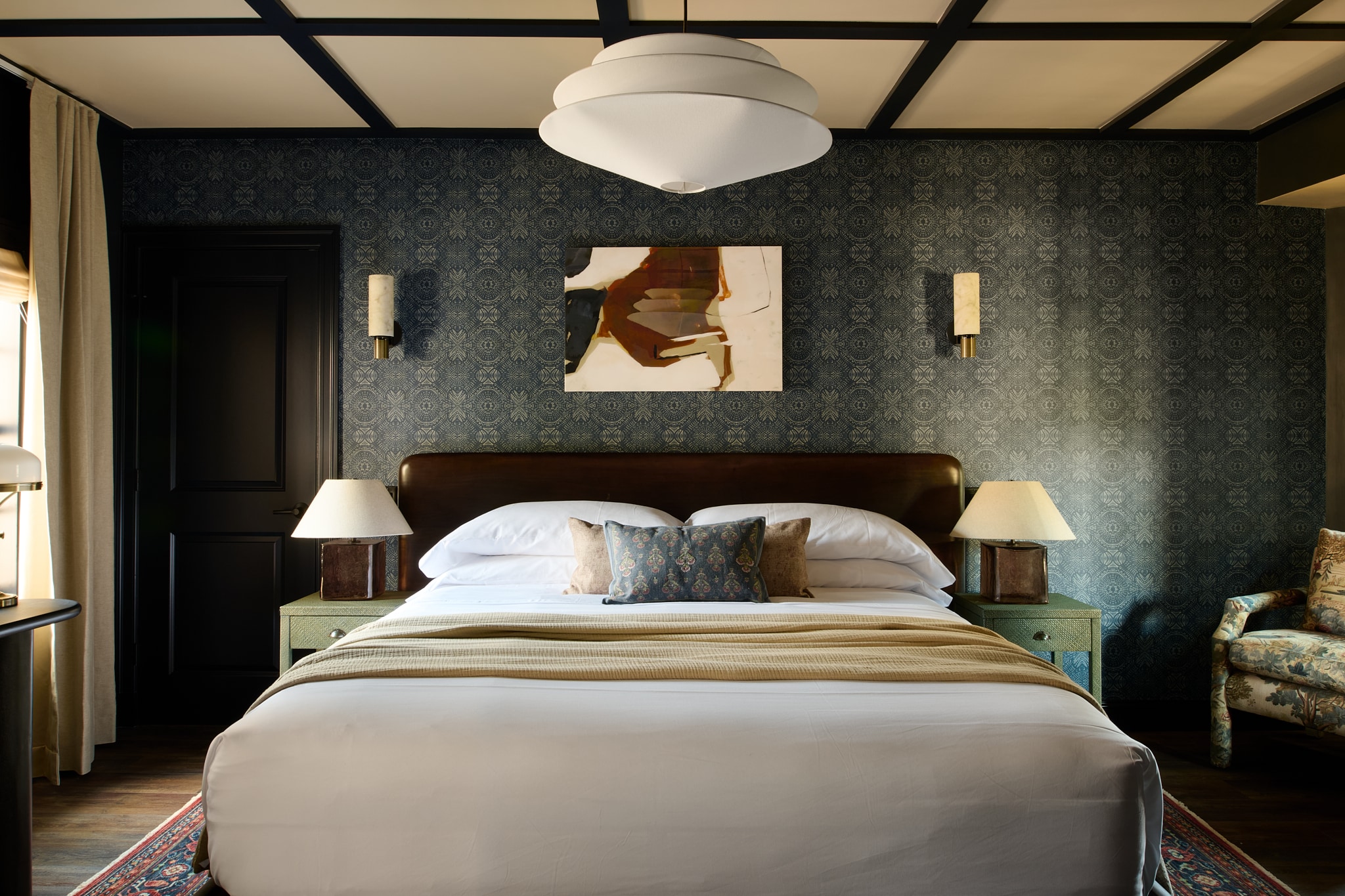 A wide view of a hotel room with a large bed, two nightstands, and a chair.