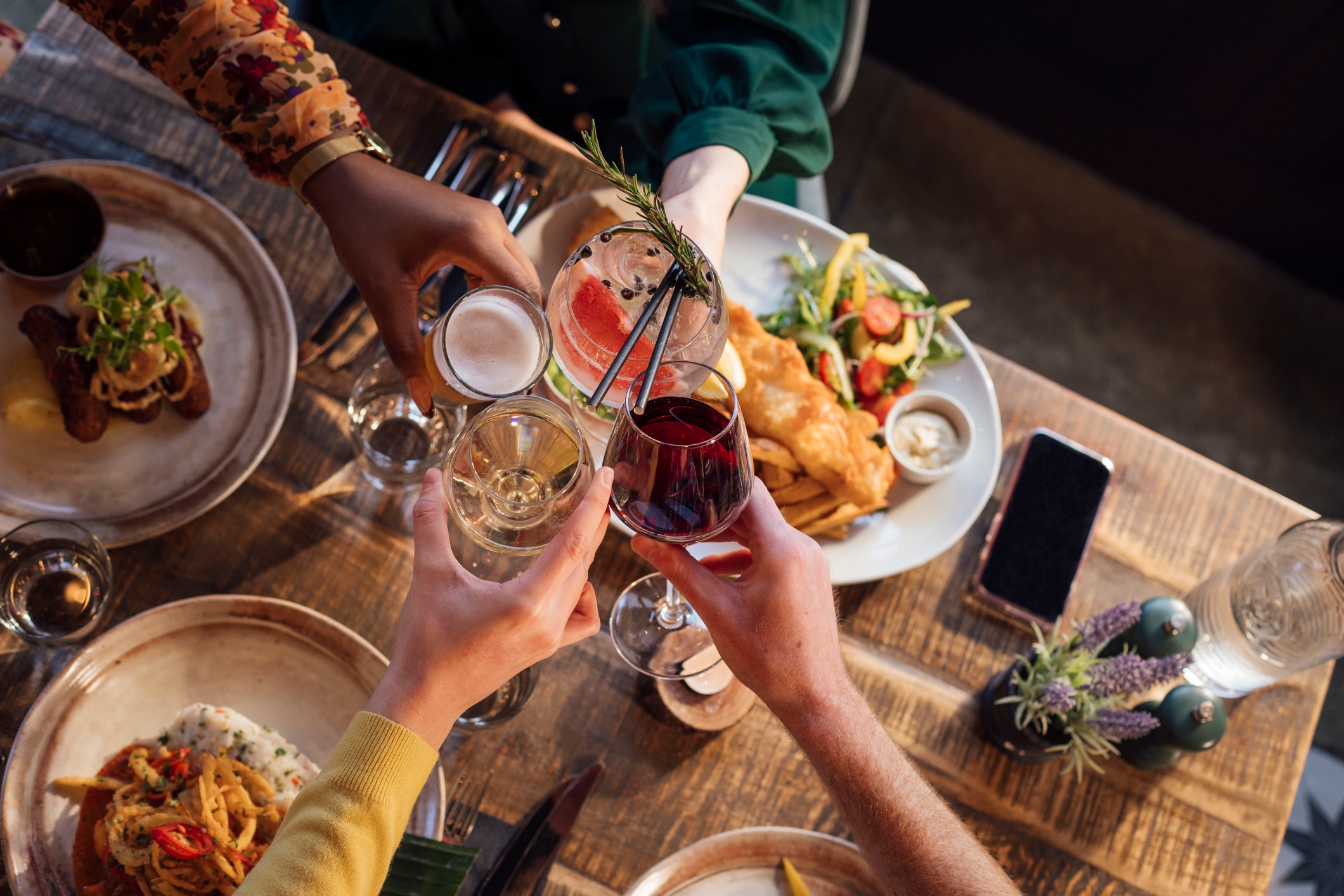 A table with food and drinks, and people clinking glasses.
