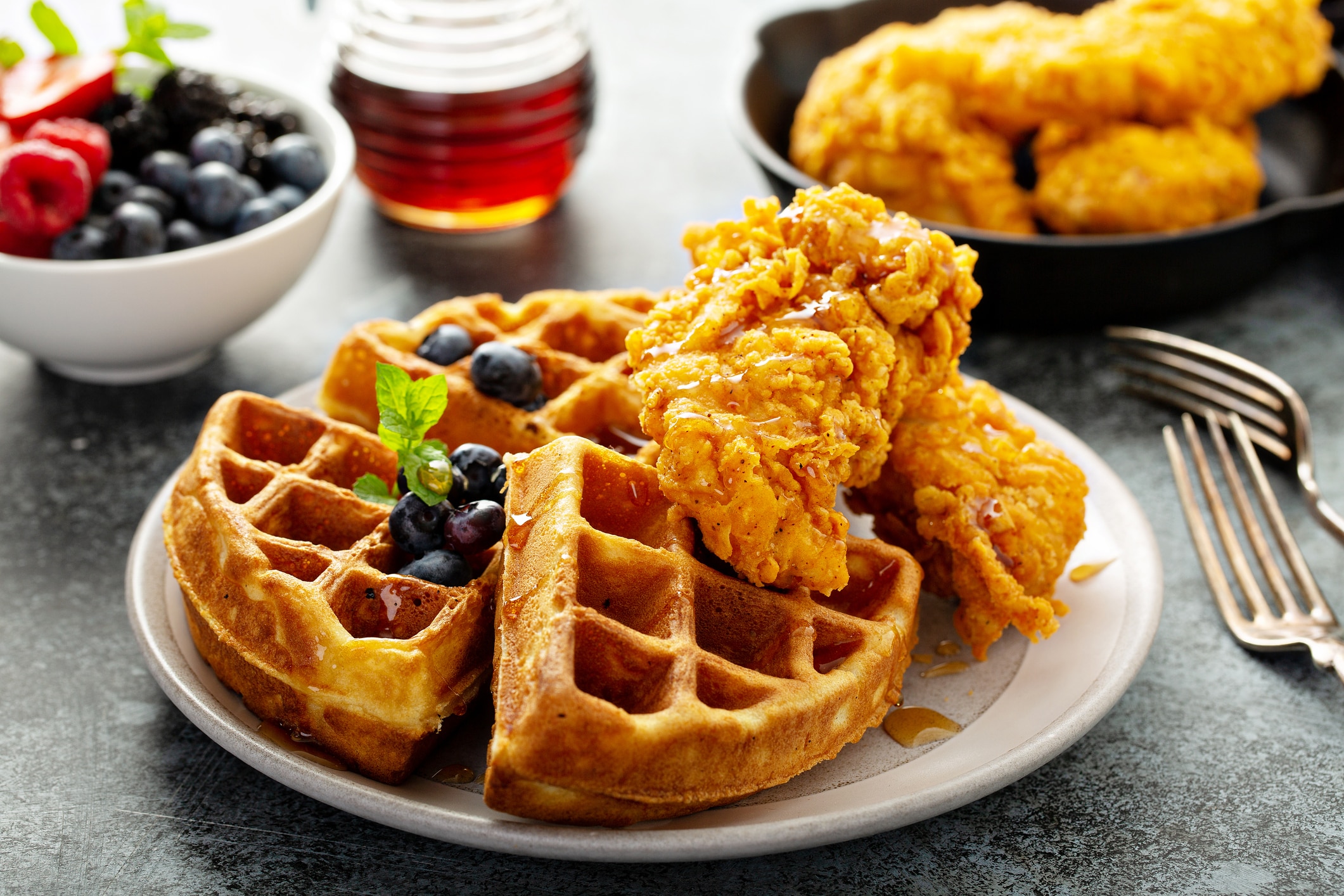 A plate of chicken and waffles with berries and syrup