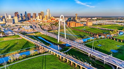 Aerial view of downtown Dallas skyline with the Margaret Hunt Hill Bridge and highway interchange in the foreground.