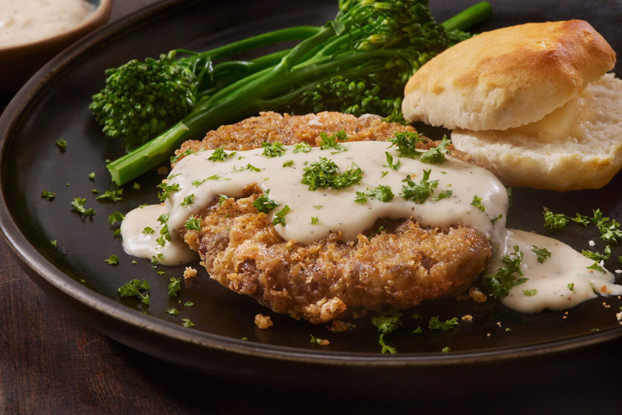 a plate of food with a piece of fried chicken, broccoli, and biscuits