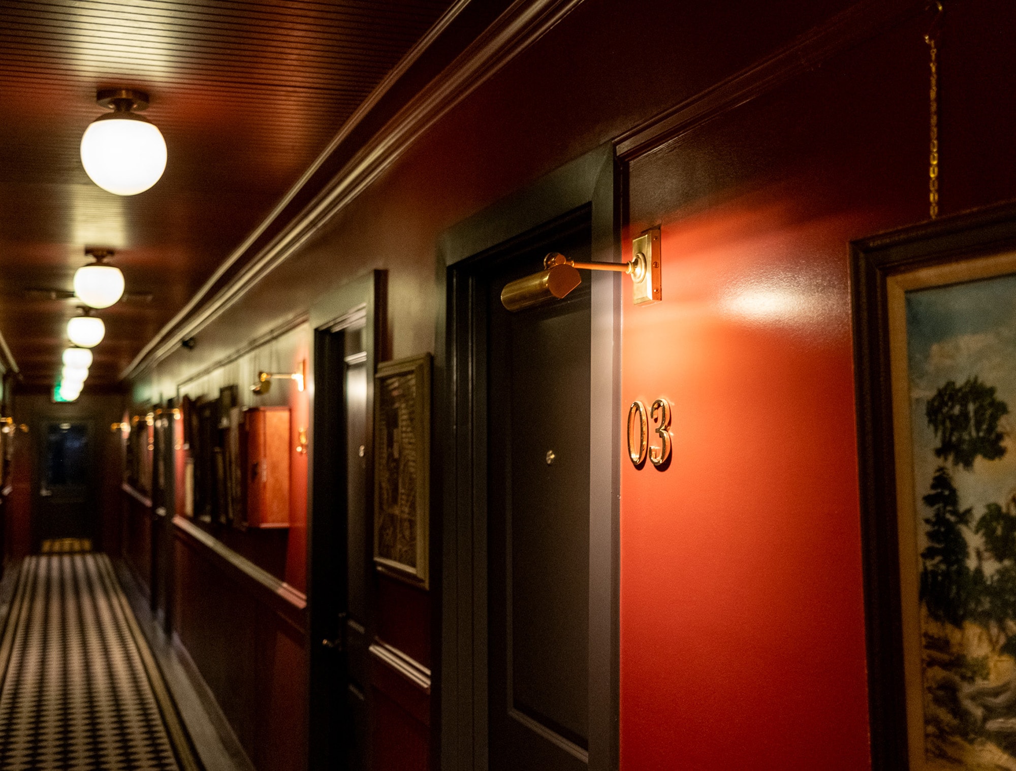 A long hallway with red walls, black and white checkered flooring, and gold lights.
