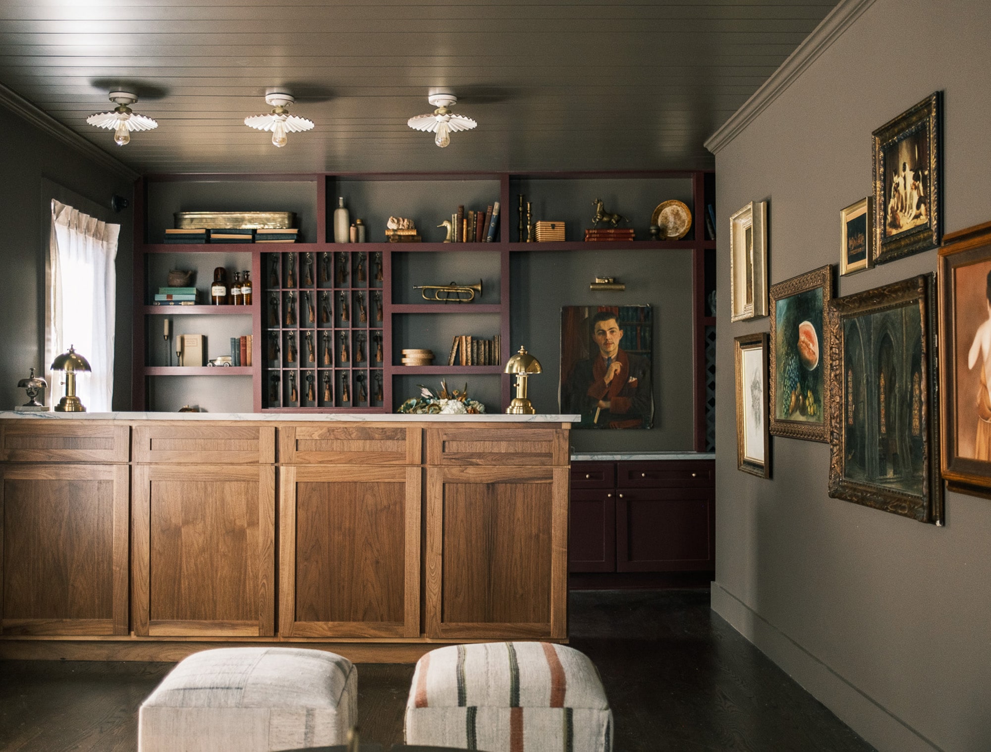 A bar area with wooden cabinets, shelves stocked with books and decorative items, and two stools in front.