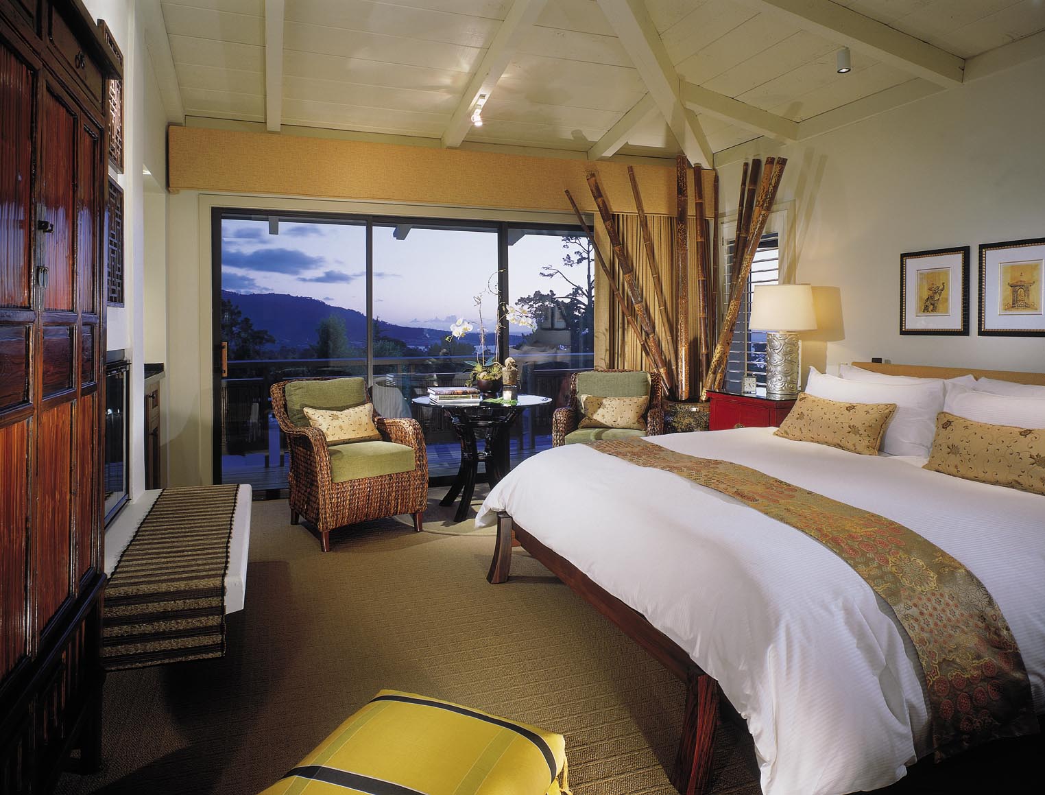 A hotel room with a large bed, two chairs, a table, and a balcony with a view.