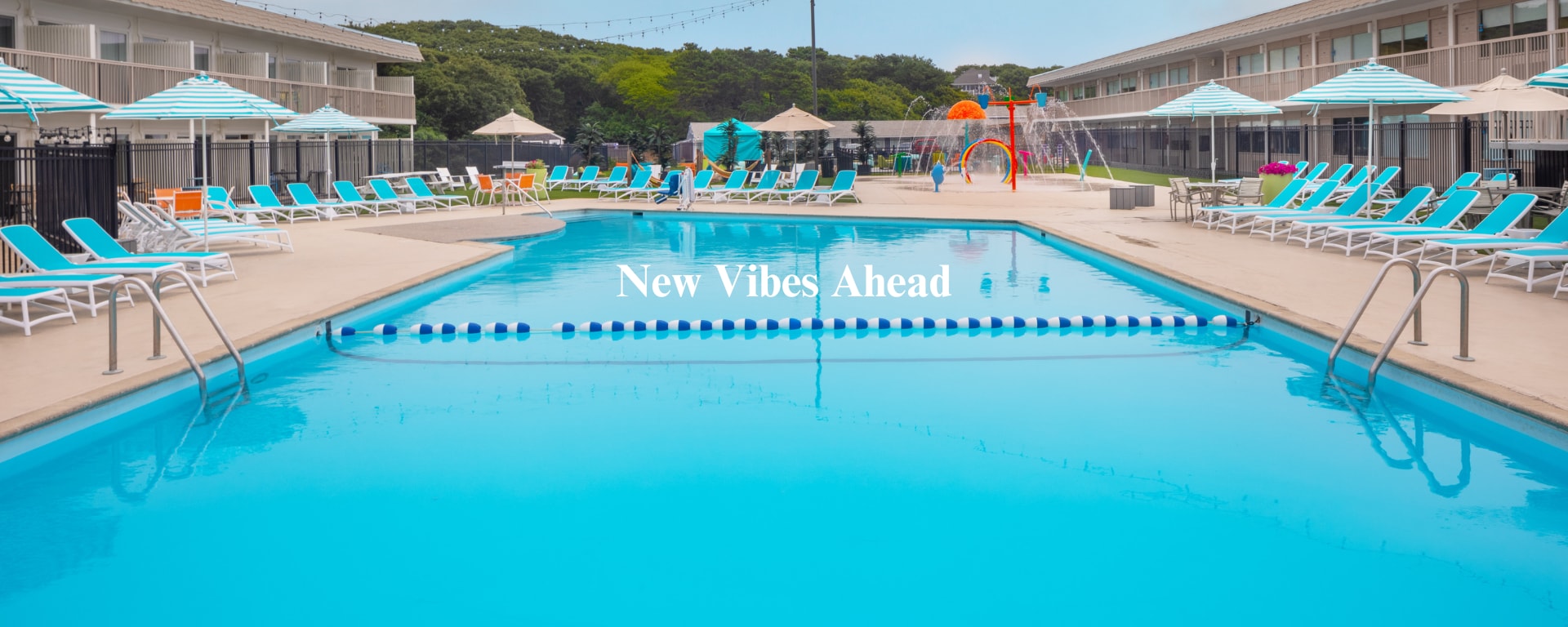 A large outdoor pool with lounge chairs and umbrellas, surrounded by buildings.