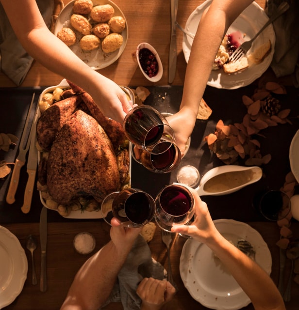 a top-down view of a Thanksgiving dinner table with people toasting with wine glasses