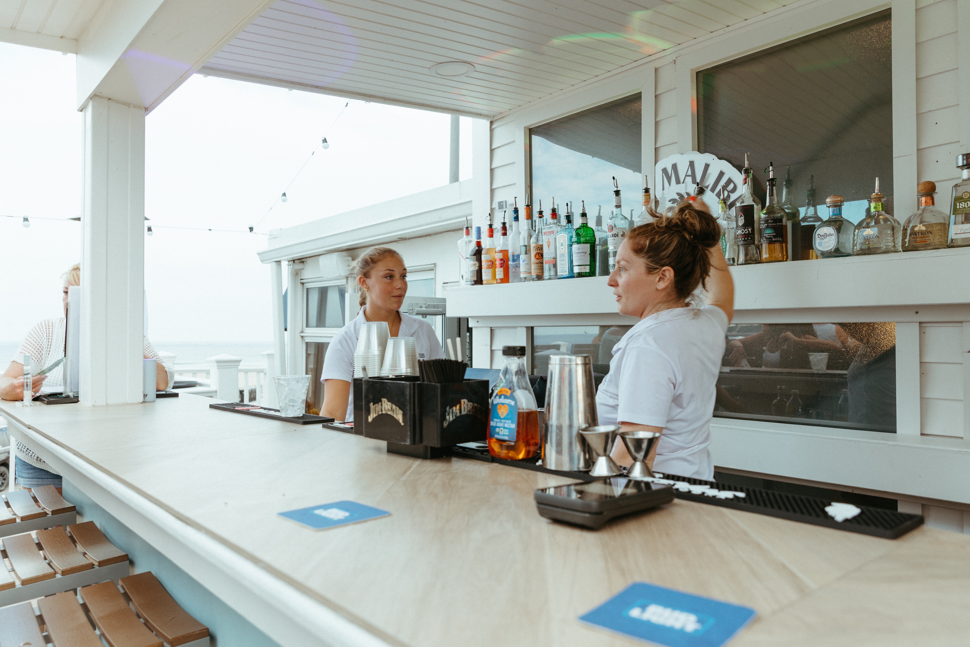 Two bartenders at a beachside bar with a view of the ocean