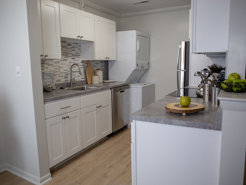 Signature Kitchen Style at California Apartments, shown here in the one-bedroom floor plan. Features white cabinetry, stainless-steel appliances, subway tile backsplash, and vinyl plank flooring.