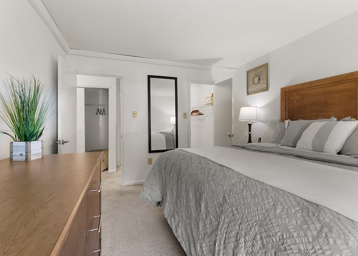 A clean bedroom with a bed, dresser and mirror at California Apartments in Absecon, New Jersey