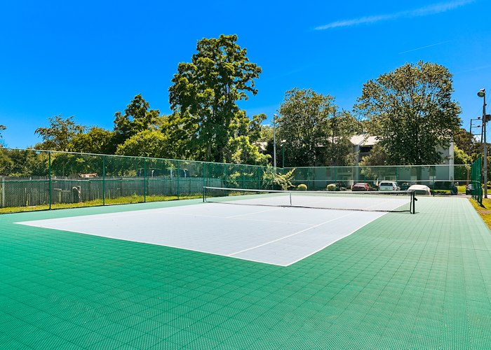 A tennis court with green grass and a fence at California Apartments in Absecon, New Jersey